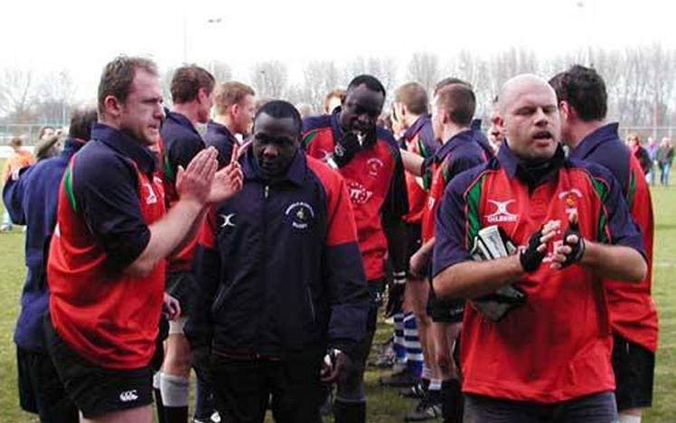 Rugby players in red and black jerseys walking on a field, some clapping, post-match.