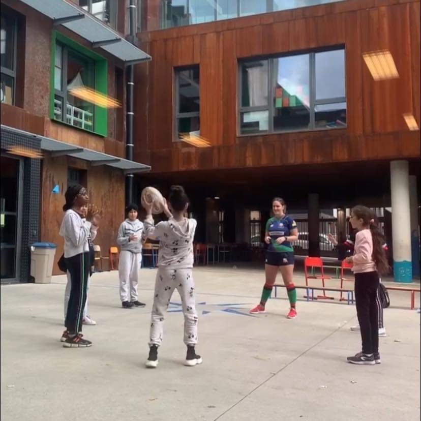 Groupe de personnes dans une cour jouant avec un ballon, entouré d'un bâtiment en briques.