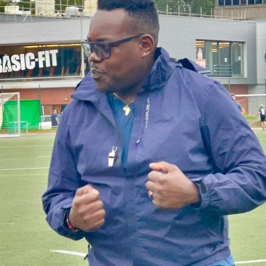 Person wearing blue jacket with whistle, standing near sports field.