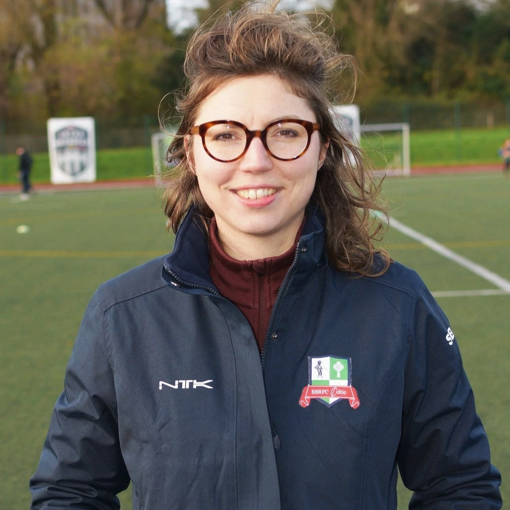 Persoon met bril en sportjack op voetbalveld