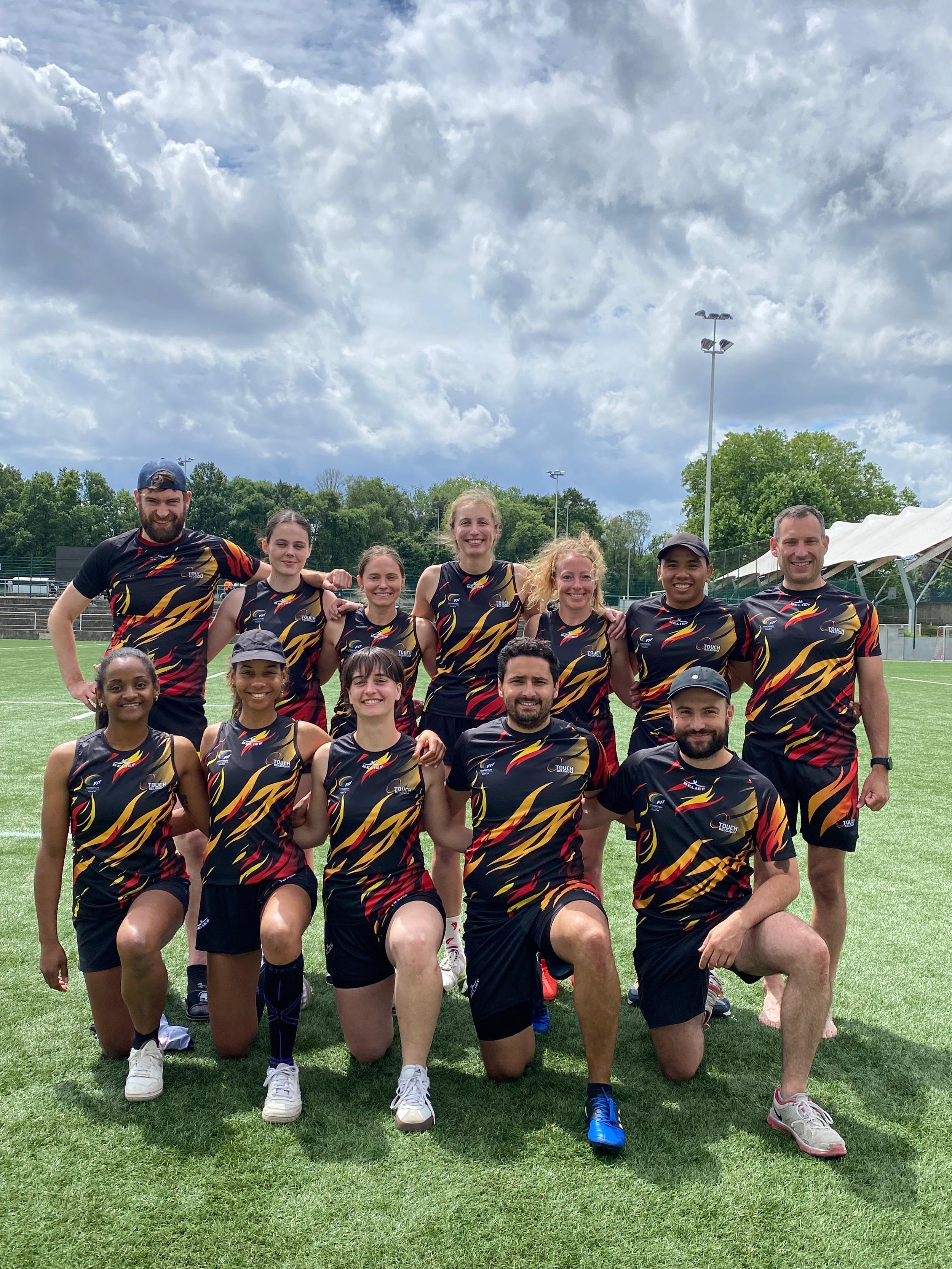 Un groupe de onze personnes vêtues de maillots de sport colorés posant sur un terrain herbeux.