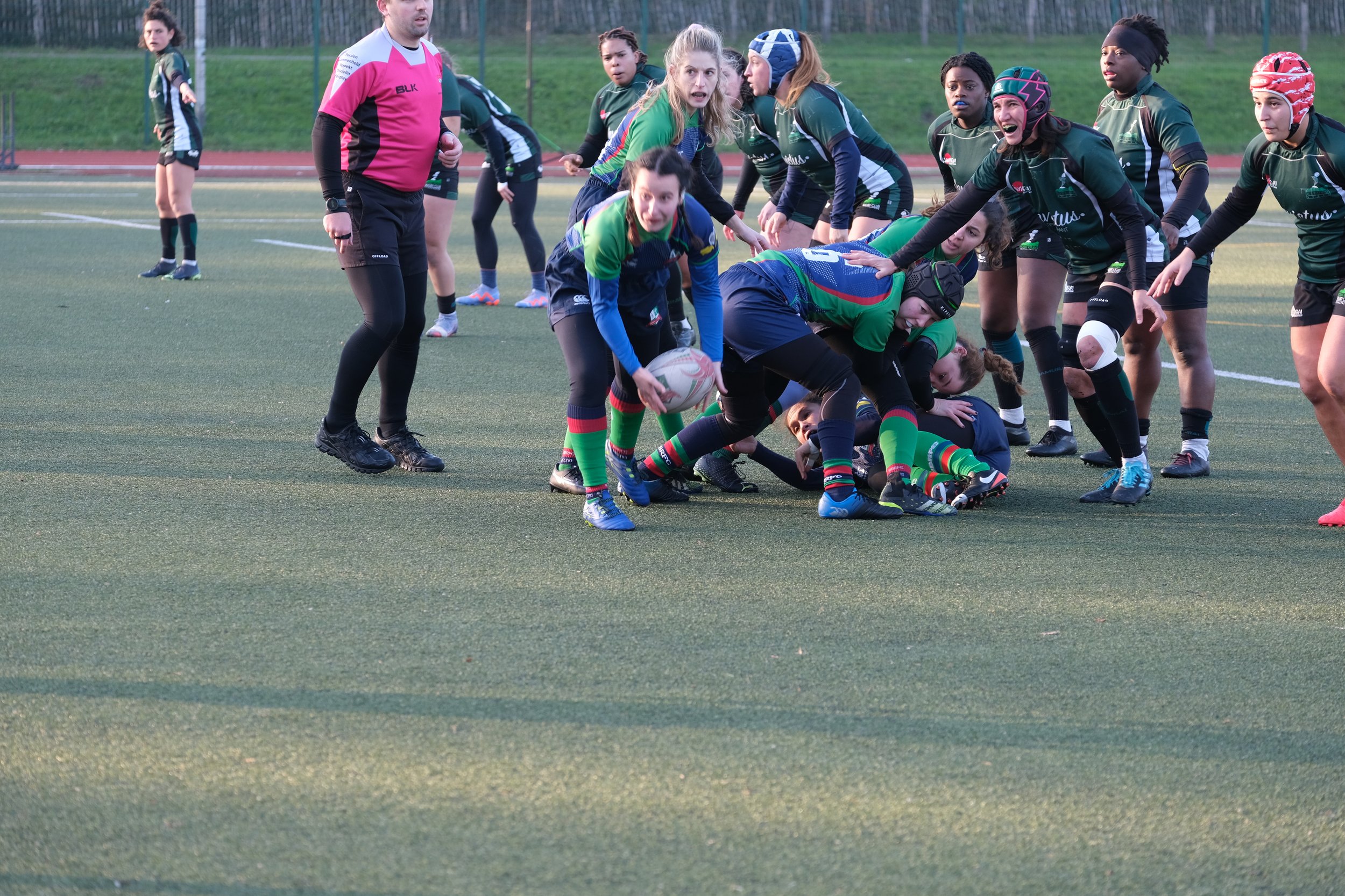 Women's rugby match with players in action, referee watching, grassy field