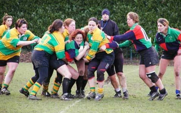 Women's rugby match with players in action, wearing colorful jerseys, and a referee in the background.