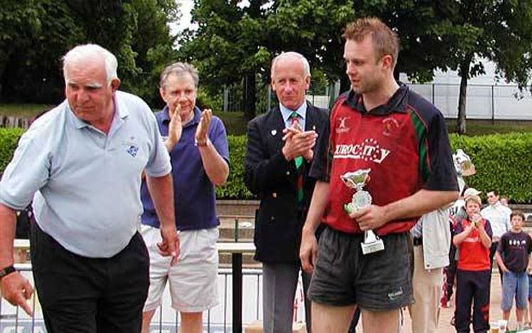 Man holding trophy with others applauding outdoors