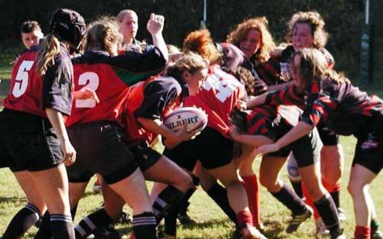 Women's rugby match in progress with players in red and black jerseys competing for the ball.