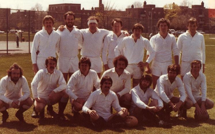 Group photo of a men's sports team in white jerseys, posed on a grassy field.