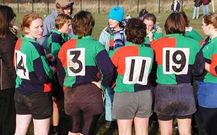 group of female rugby players in colorful jerseys with numbers, standing on a field
