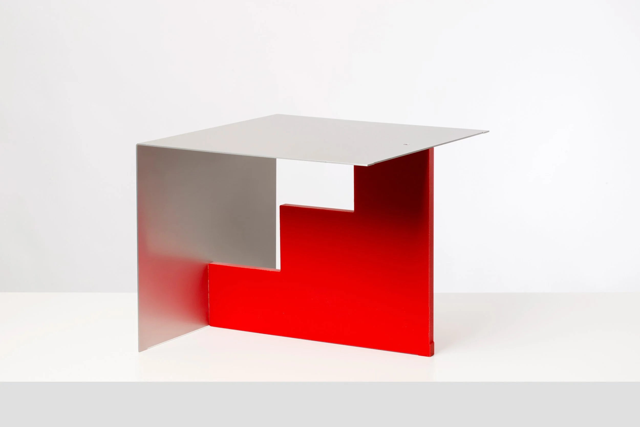 Modern desk with geometric design, featuring a red base, gray side panel, and a white desktop, set against a plain white background.