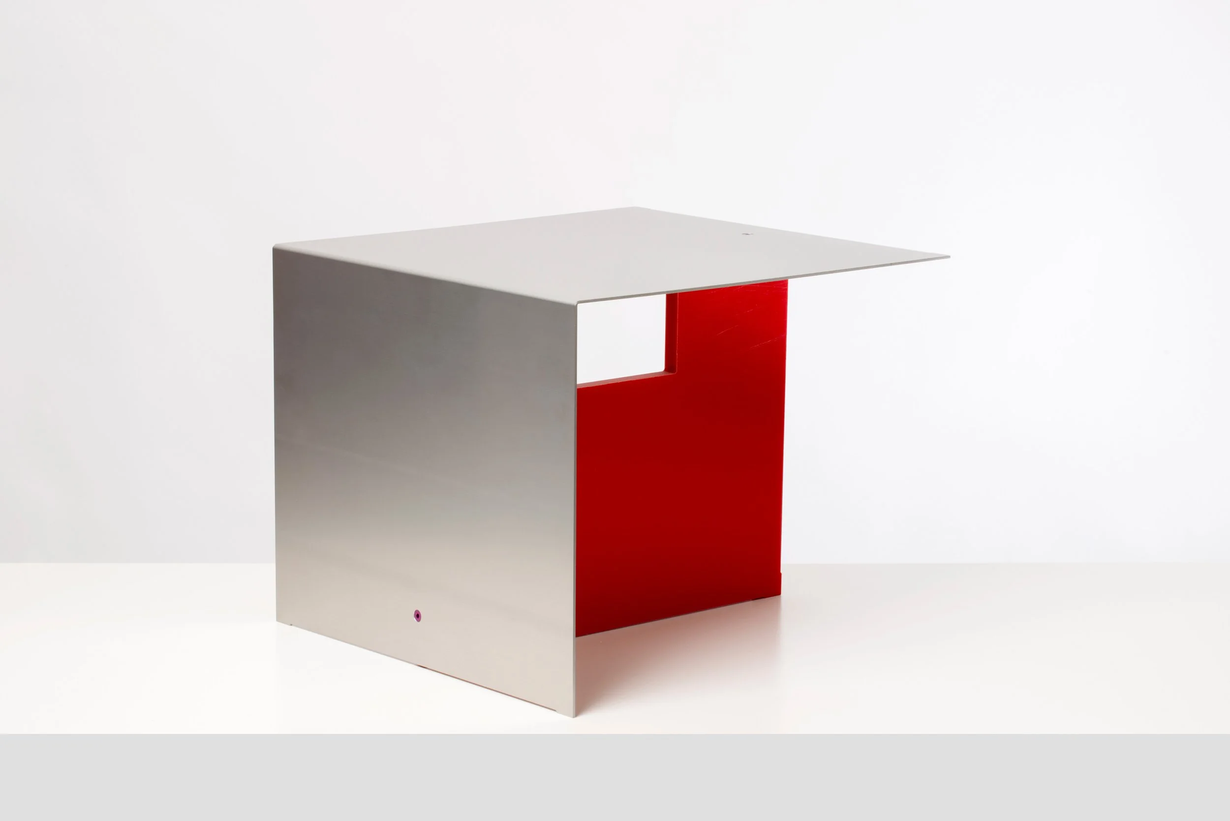 Minimalist desk with a gray top and red side panel, set against a white background.