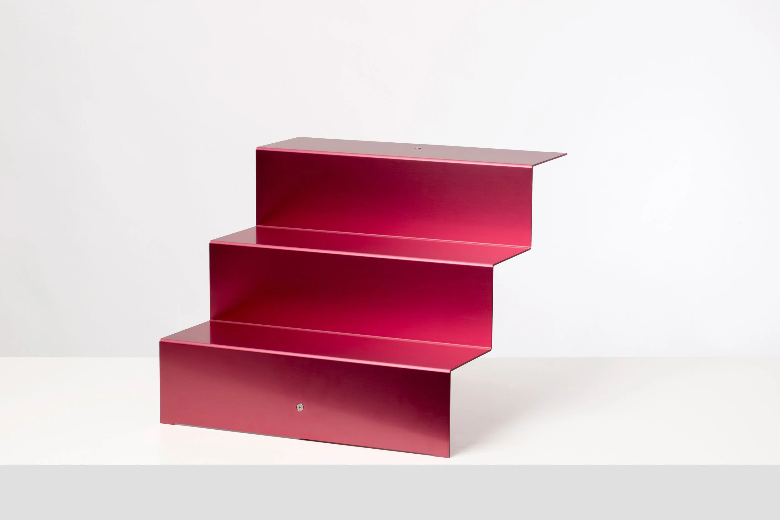 A modern, pink metal staircase with three steps, set against a plain white background.