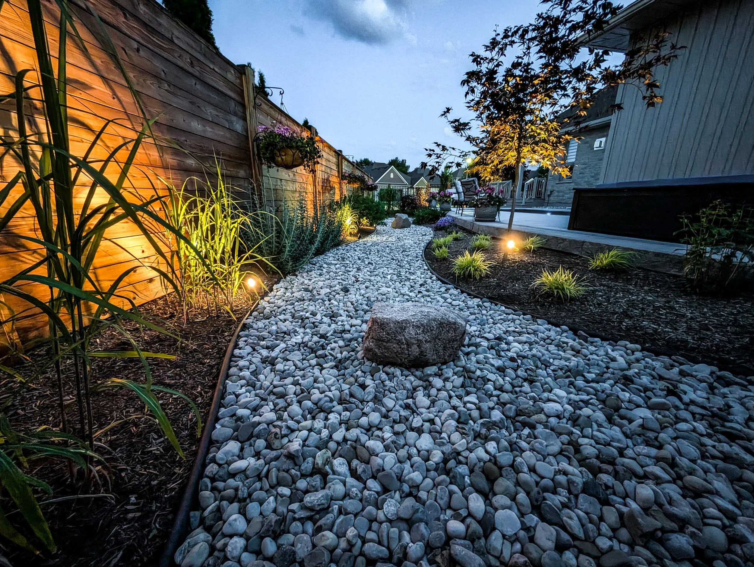 Custom landscape lighting brings this backyard garden, stone pathway and surrounding plantings to life after dark.