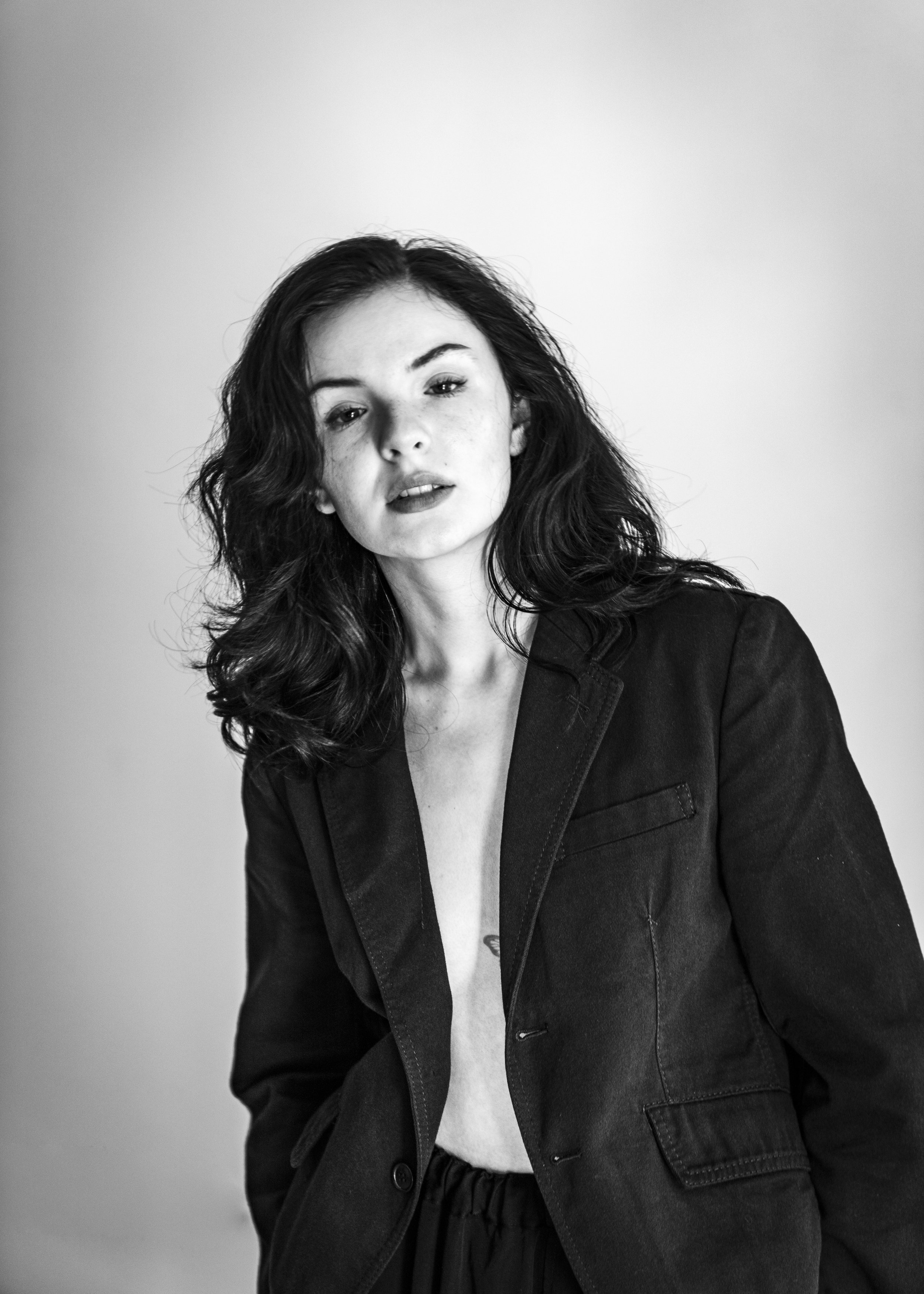 Black and white portrait of a young woman with wavy hair, wearing a denim jacket and a white shirt, looking slightly to the side with a serious expression.