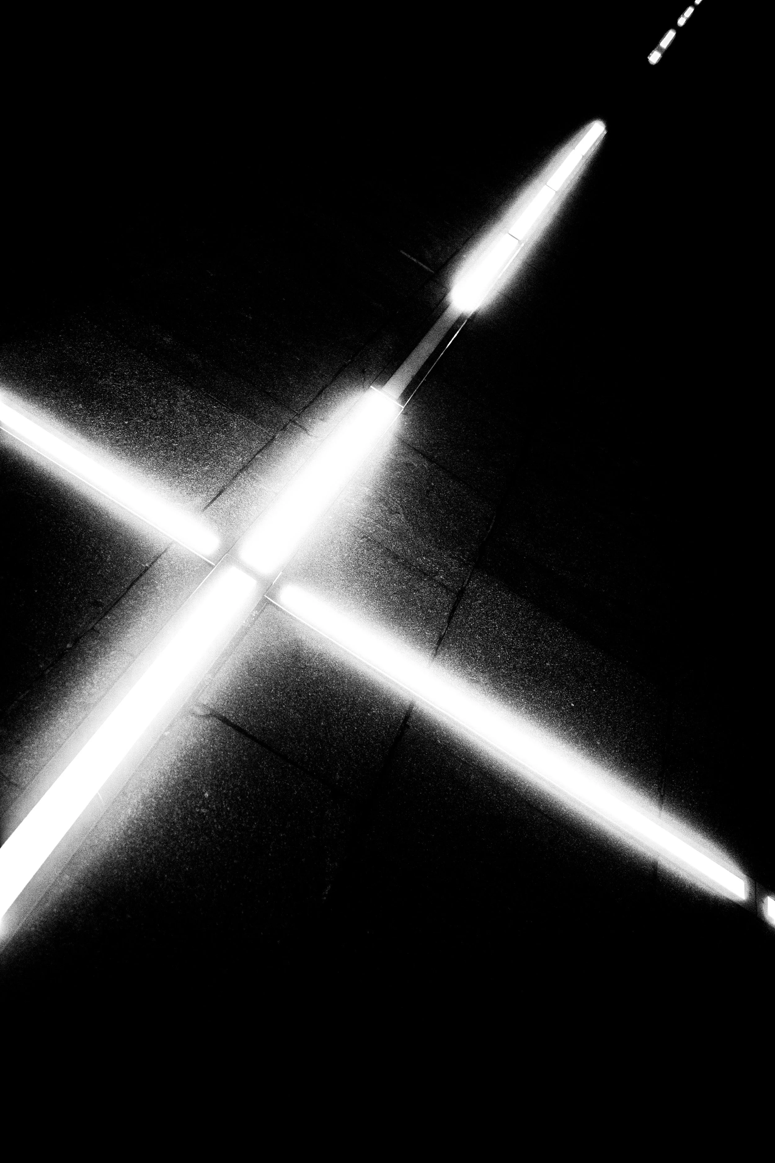 Black and white photo of illuminated horizontal lines and vertical light strips on a dark floor, creating a geometric pattern.