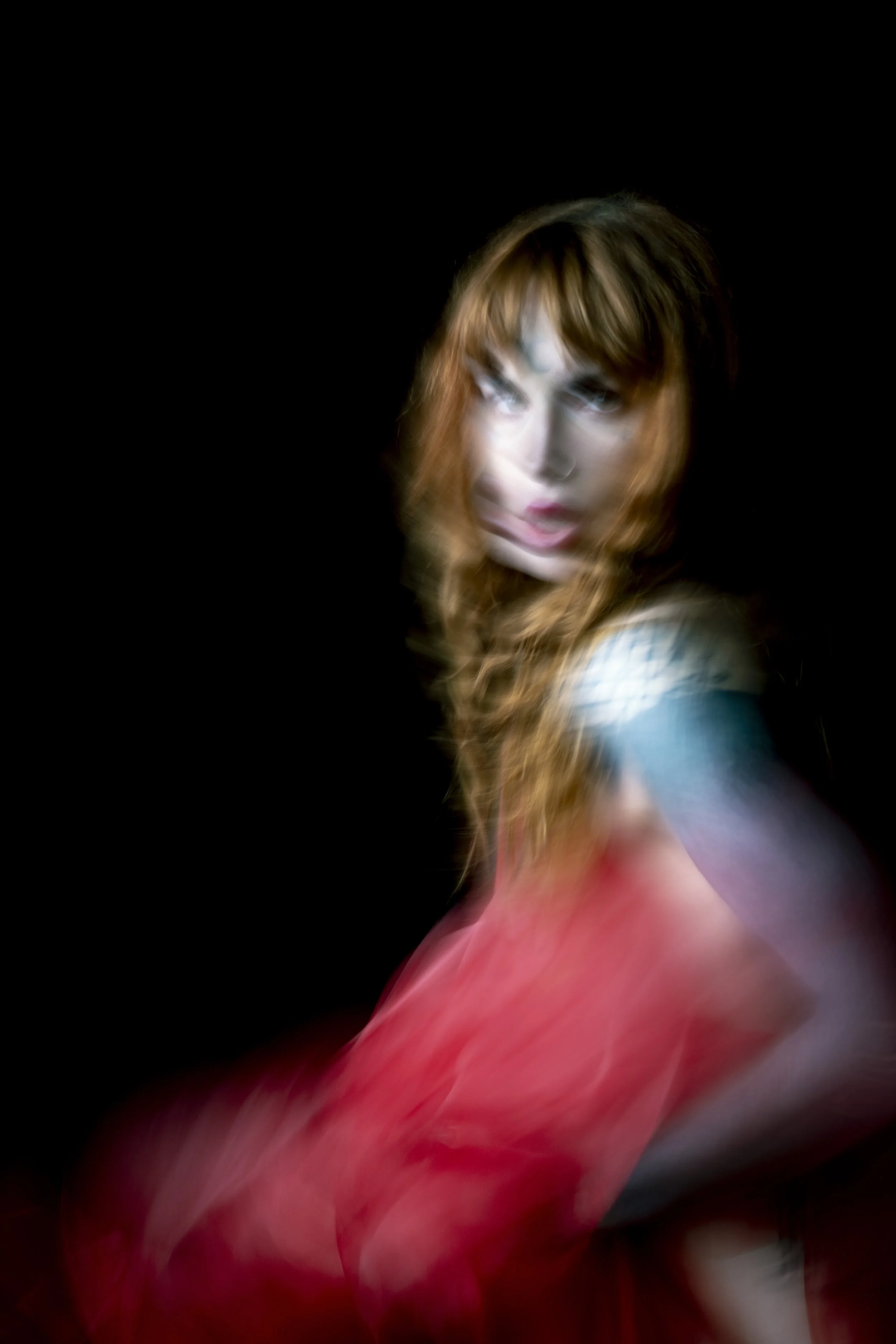 Blurry portrait of a woman with long, wavy reddish hair against a black background.