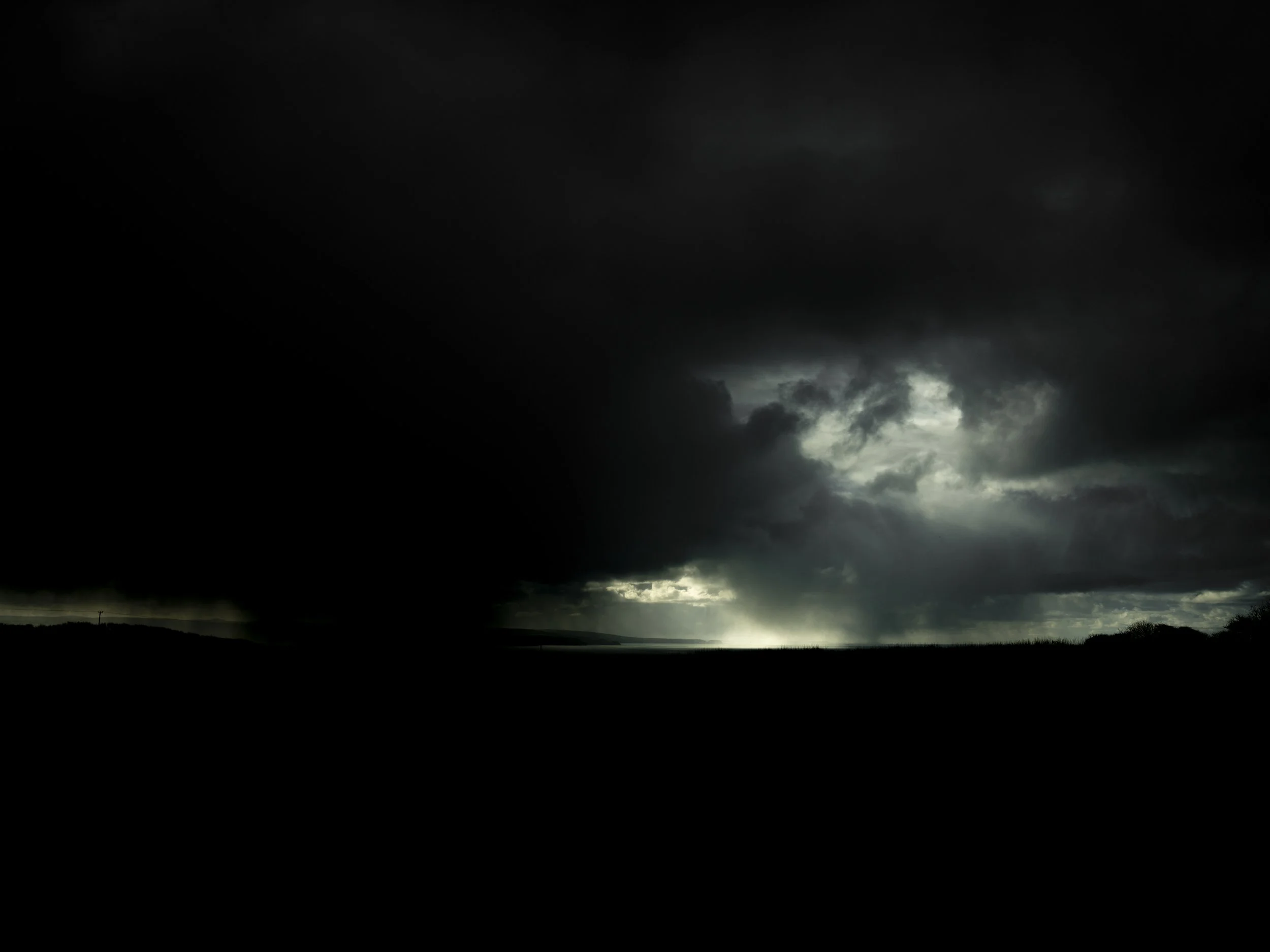 Dark storm clouds over a landscape with rain and a cloudy sky.