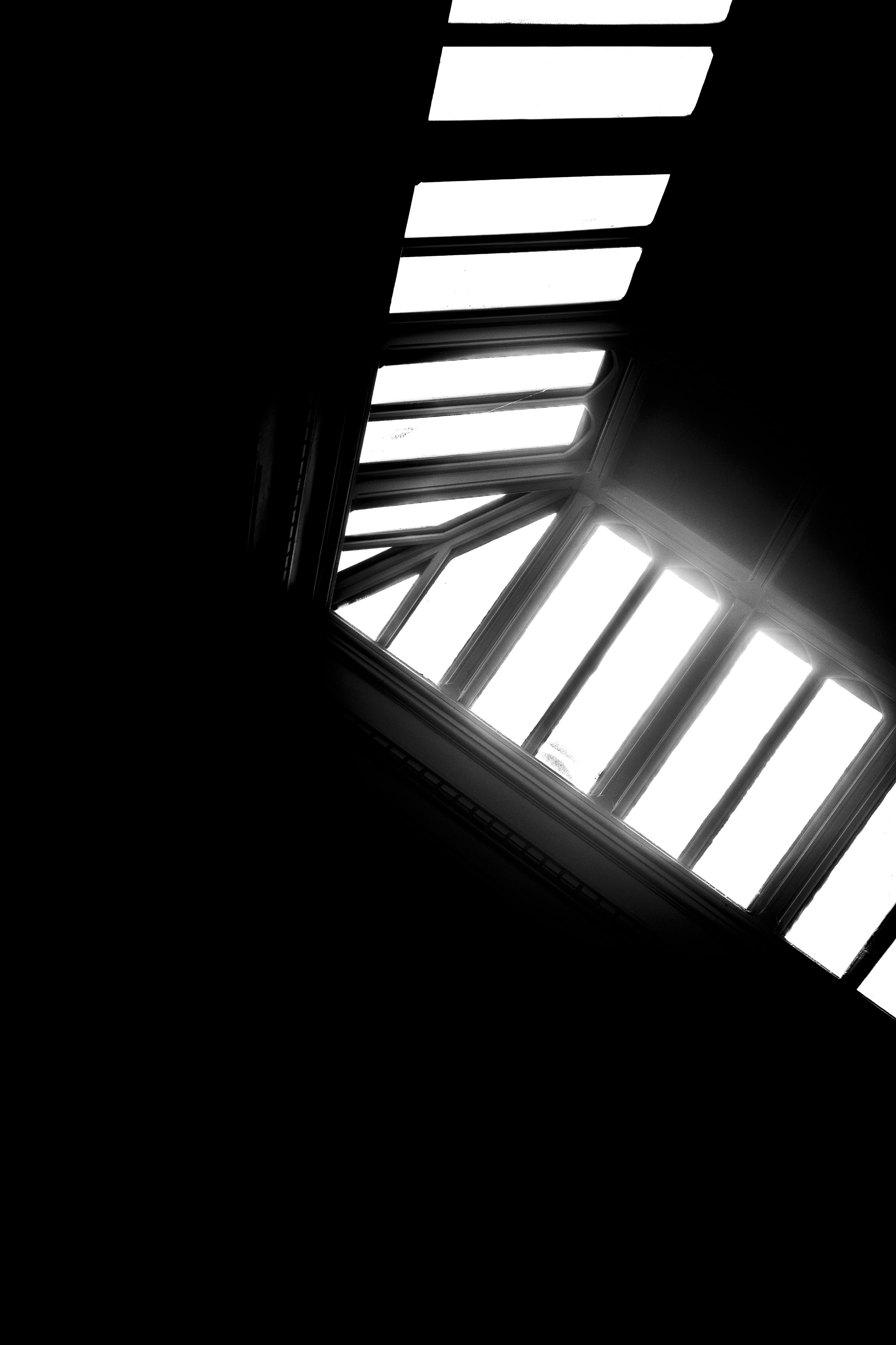 Black and white photo of a window with multiple rectangular panes, some of which are open, revealing a cloudy sky outside.