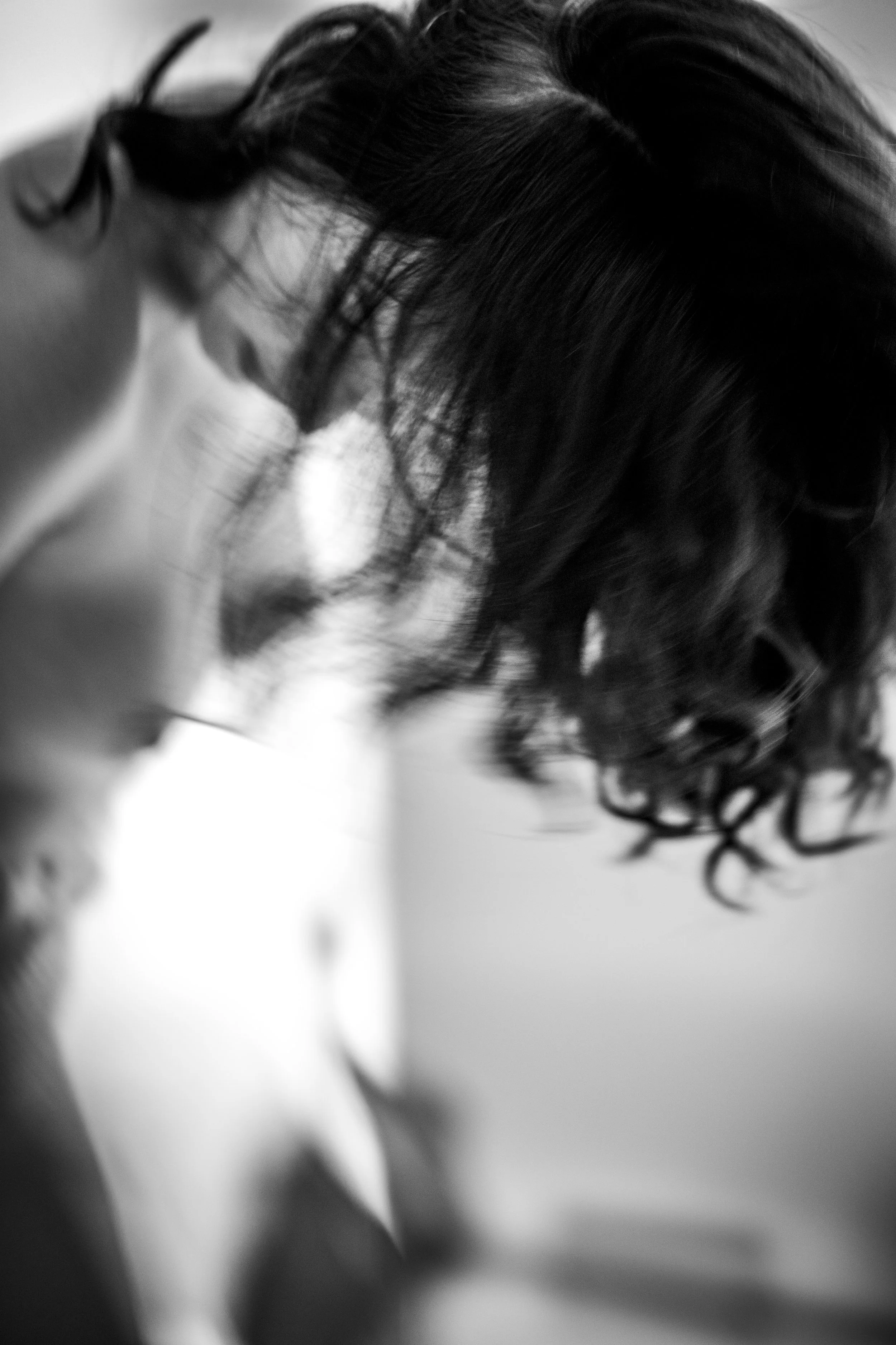 Close-up black and white photograph of a woman with dark wavy hair, her eyes closed, resting her head on a surface.
