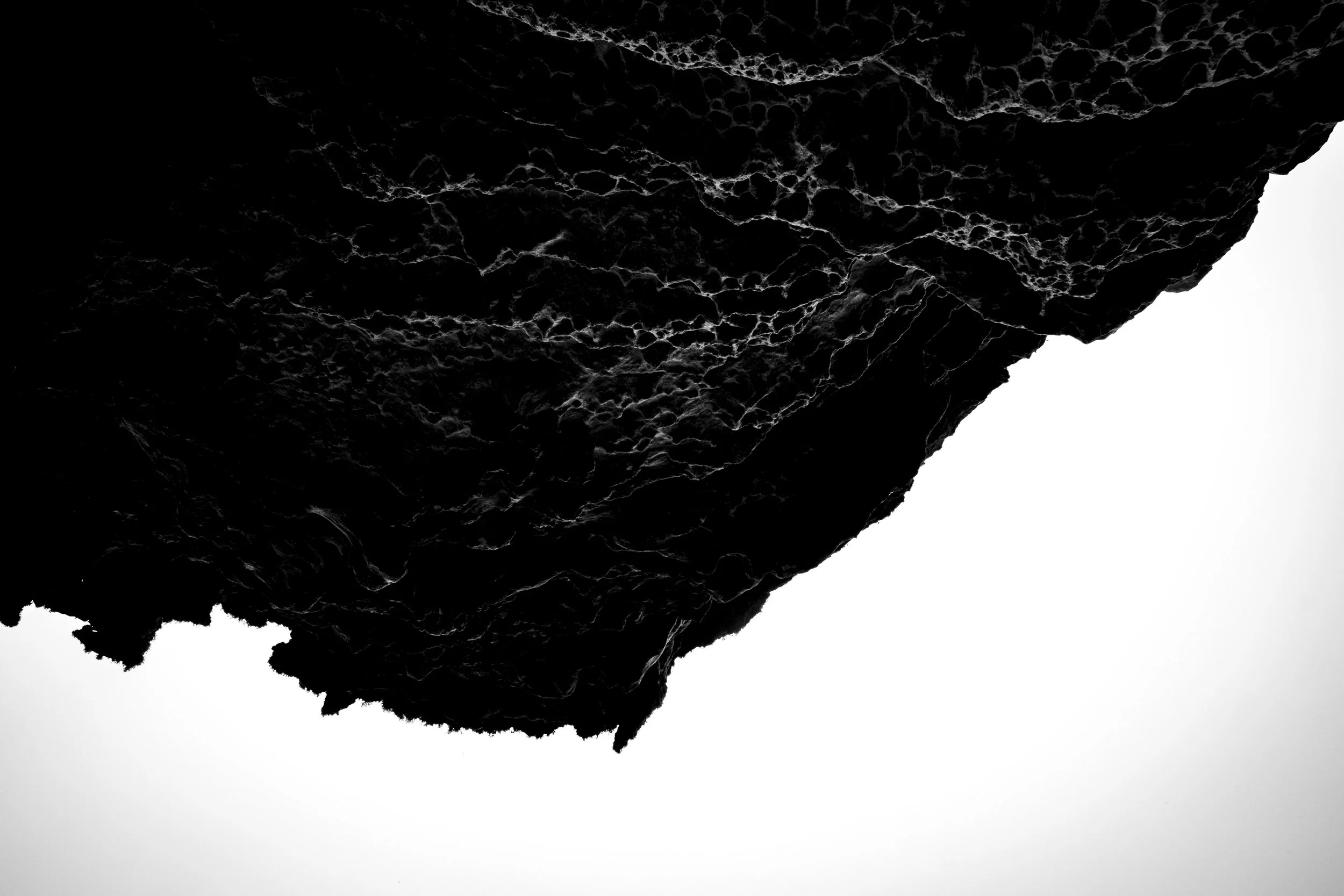 Black textured rock or volcanic surface with white cracks and patterns against a white background.