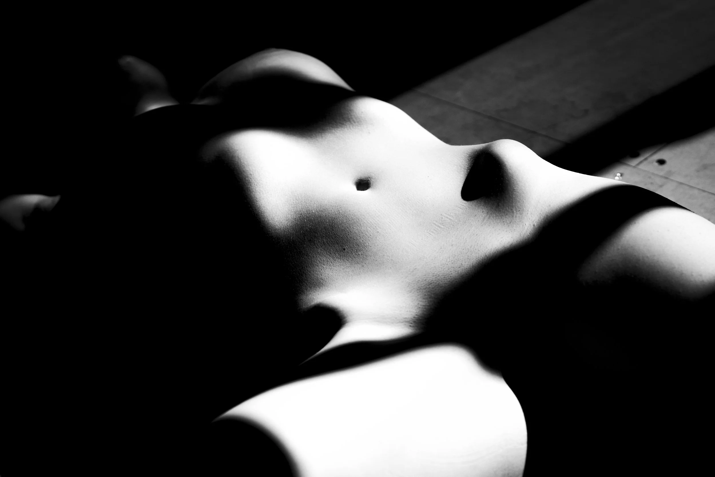 Black and white abstract photograph of a female torso lying on the floor with shadows cast across the body.