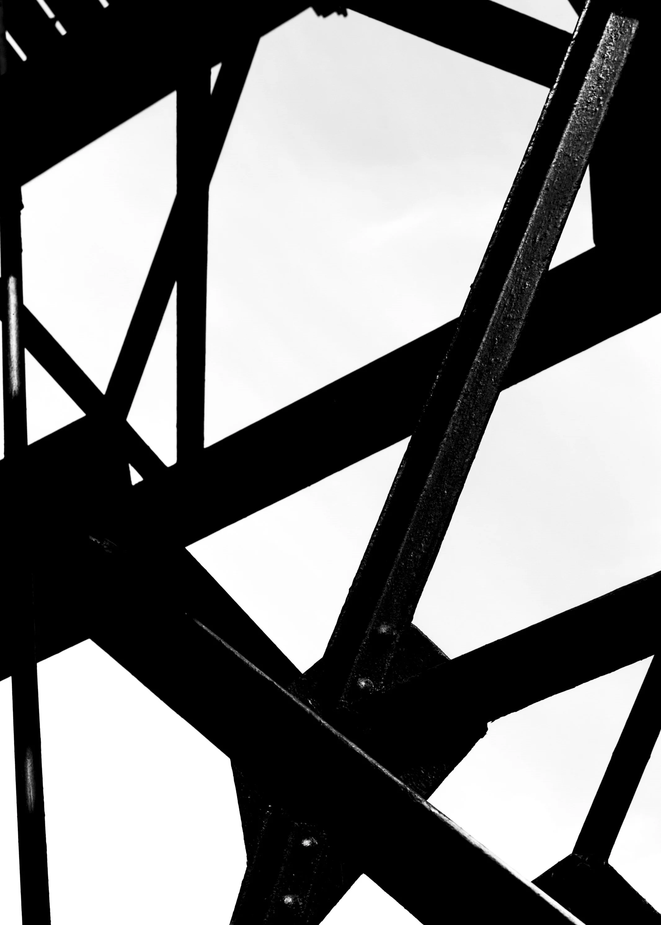 Black and white photo of a metal structure, possibly part of a ladder or scaffolding, viewed from below against a cloudy sky.