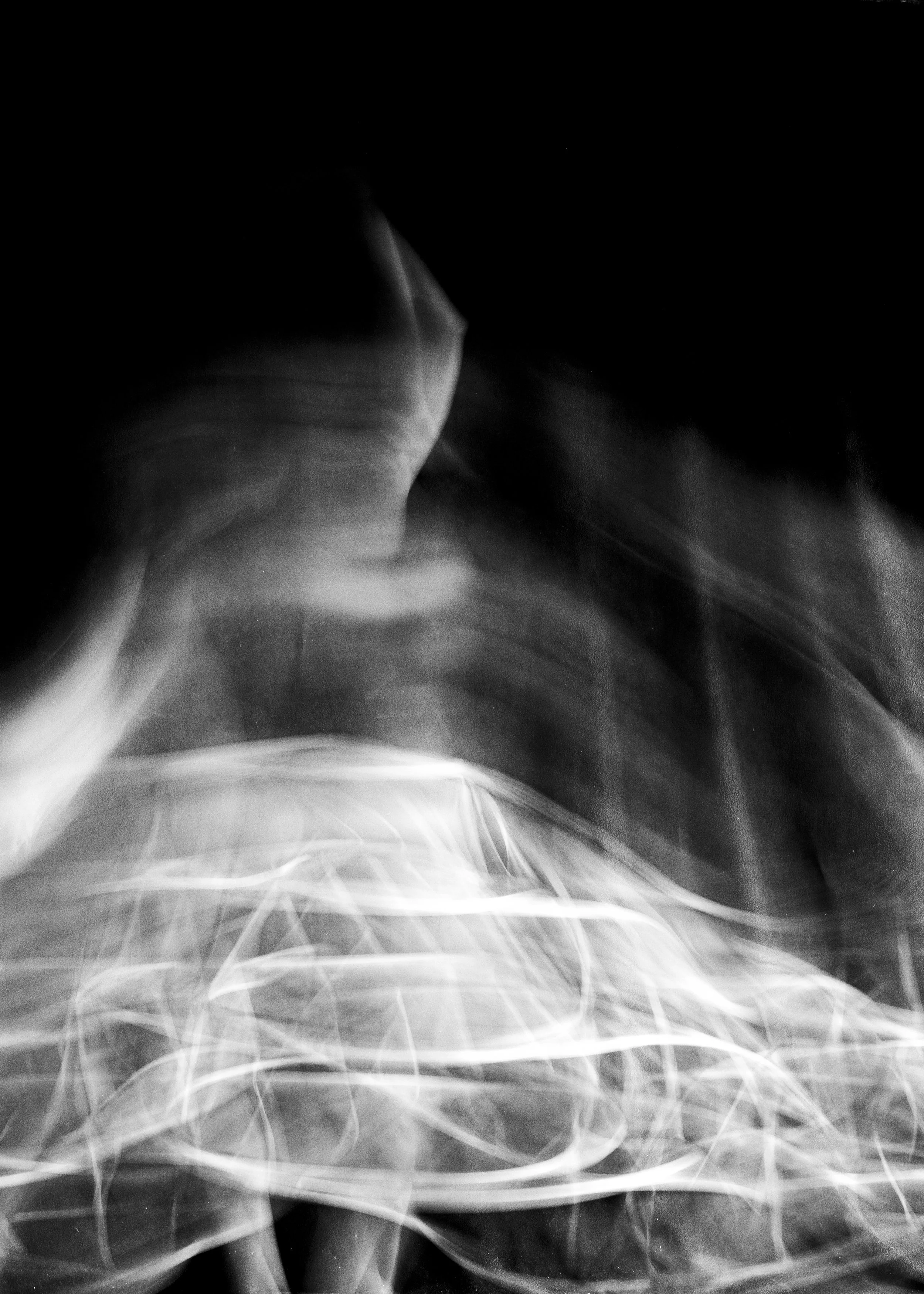 Abstract black and white photo with swirling light trails and a faint silhouette of a hand reaching upward.