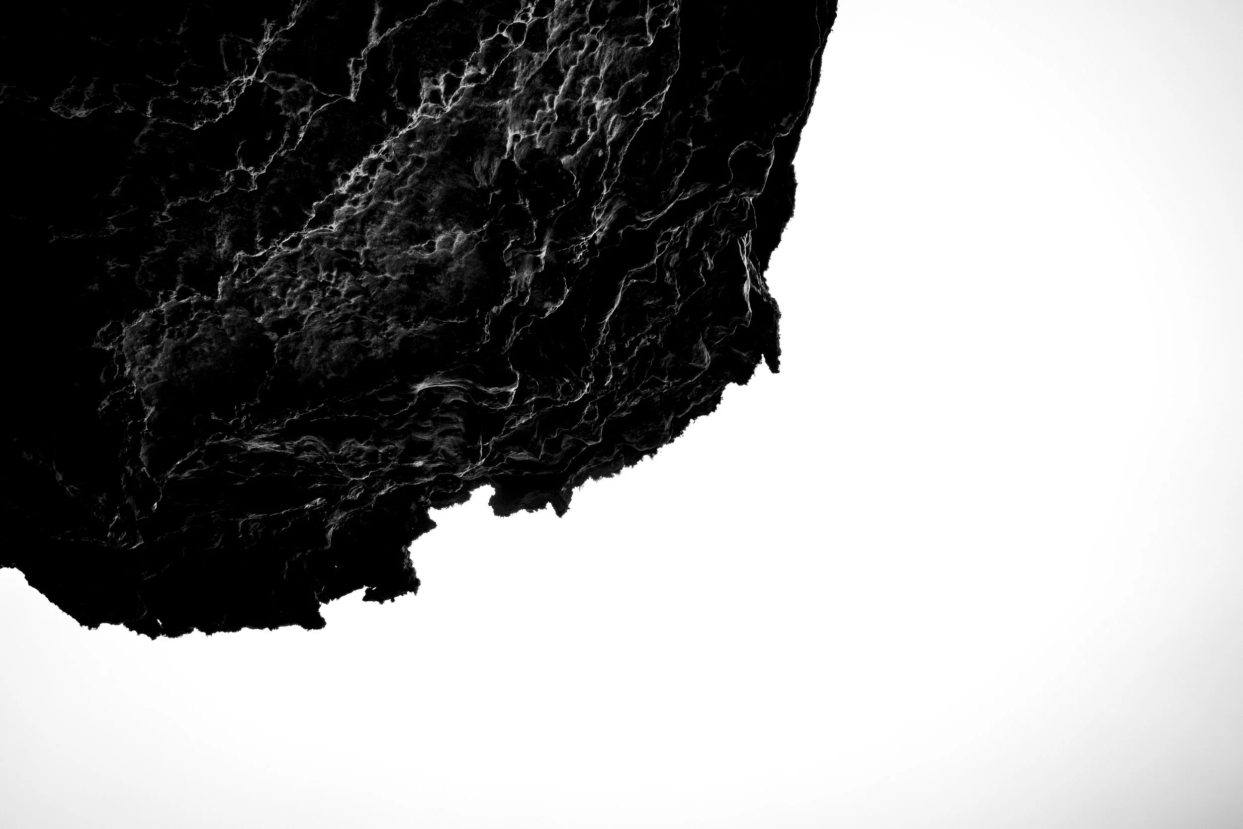Close-up of a dark, rough, textured rock surface with white veins and cracks, partially obscured by a white background.