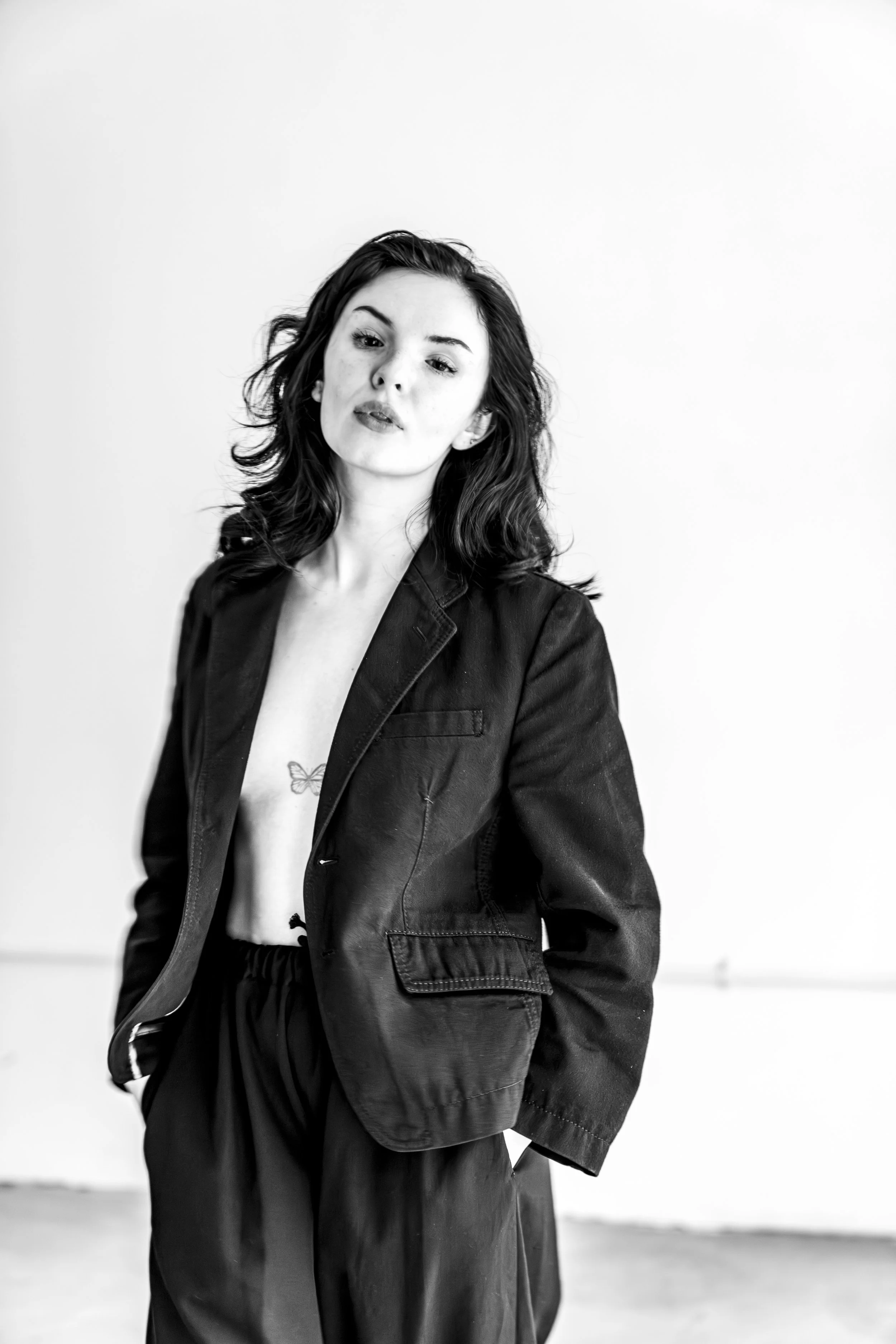 Black and white photo of a woman with dark wavy hair, wearing a leather jacket, standing against a plain background.