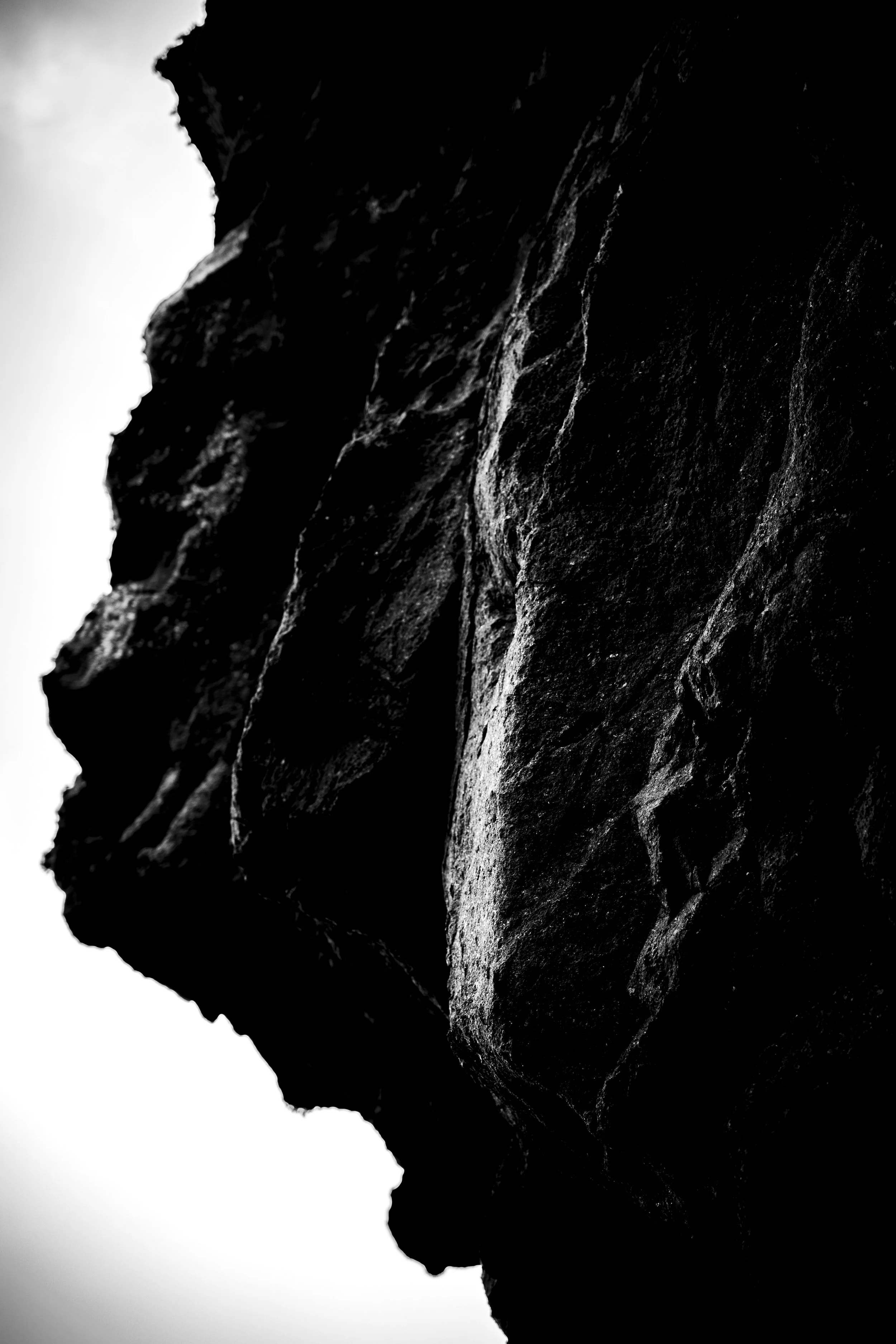 Close-up of a dark, textured rock formation with sharp edges and layered surface in black and white.