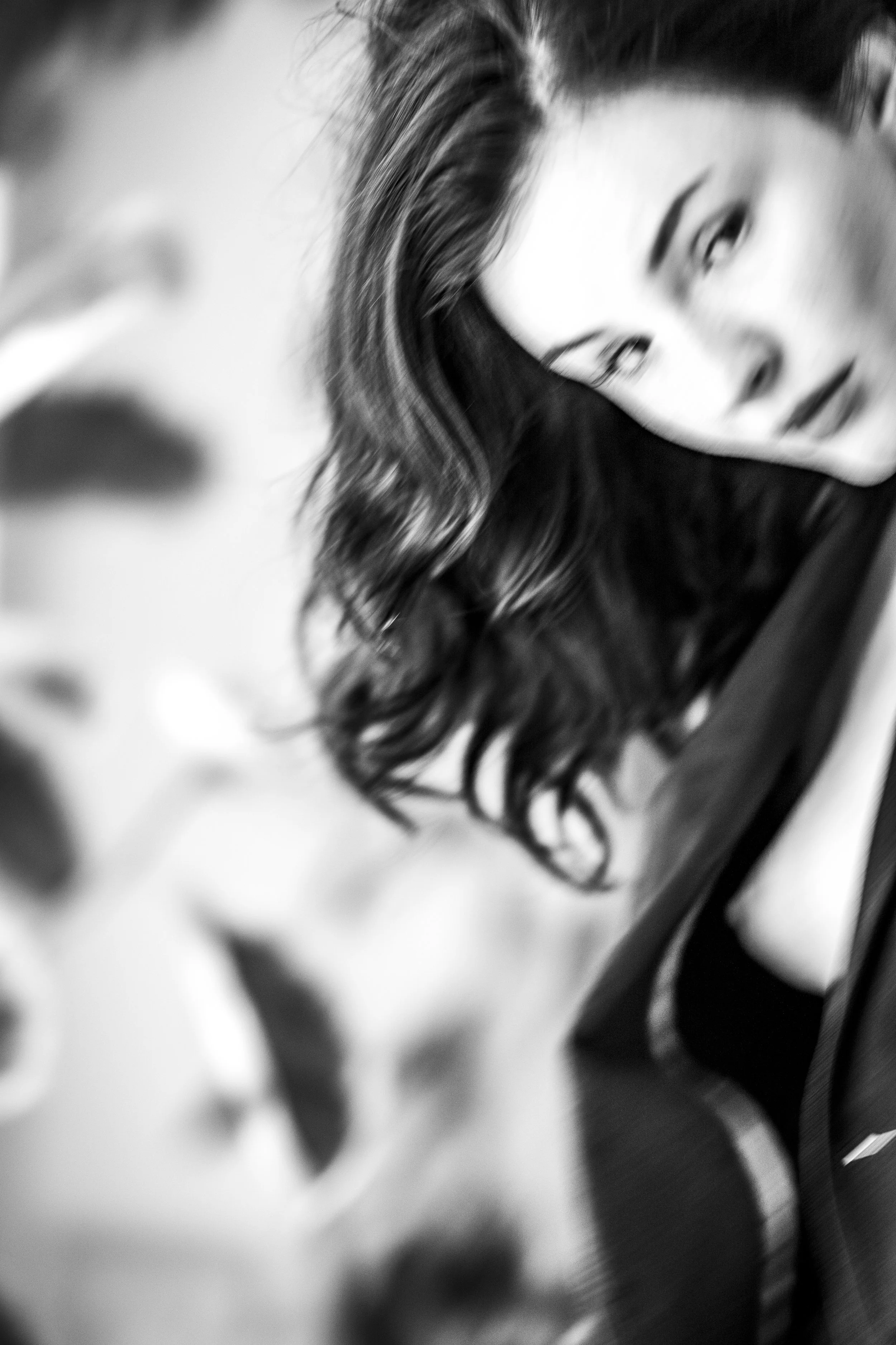 A black and white close-up photograph of a woman with wavy hair, looking slightly to the side, with a blurred background.