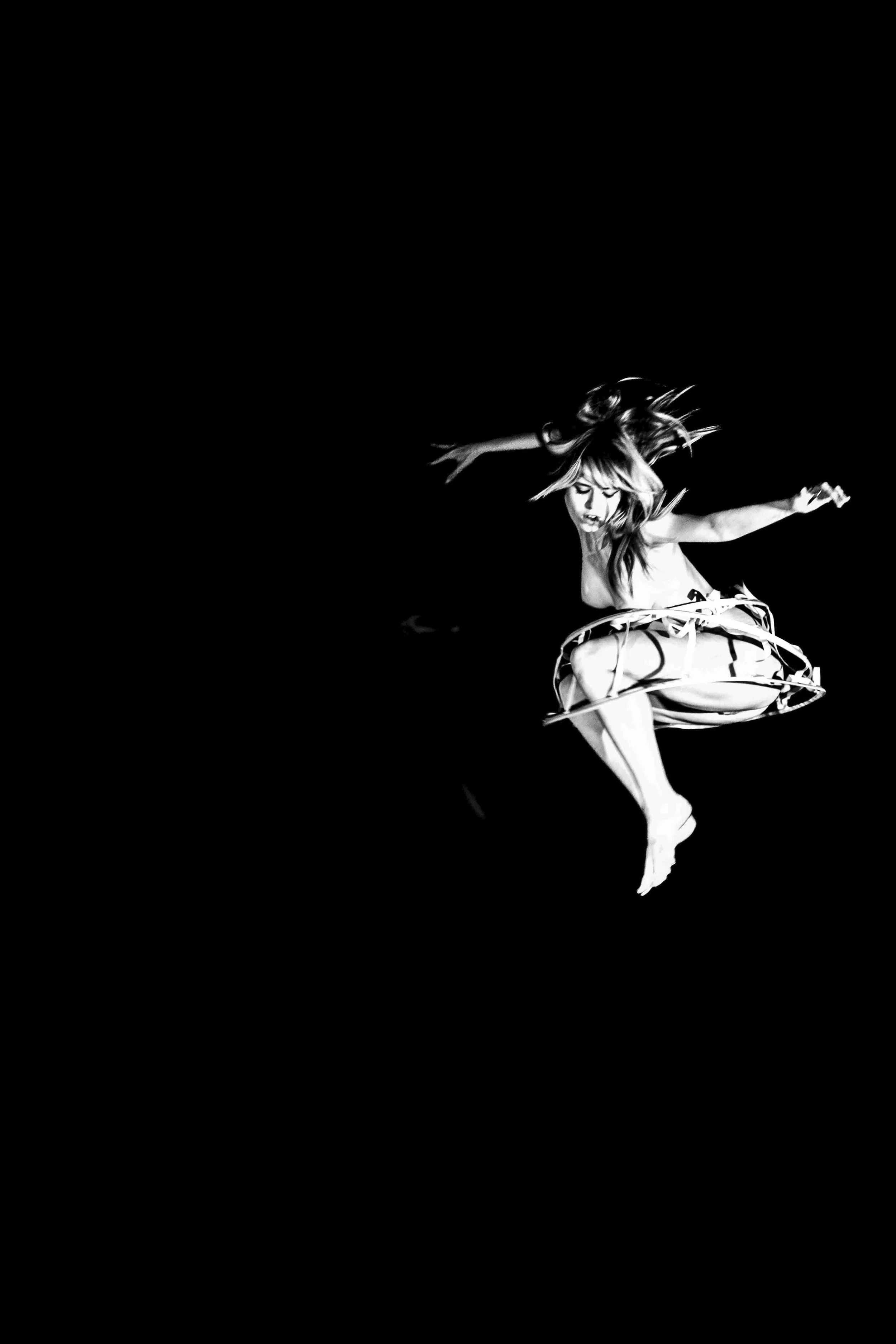 A woman gracefully jumping with her arms outstretched inside a dark space, wearing a dress with a circular skirt and high heels.