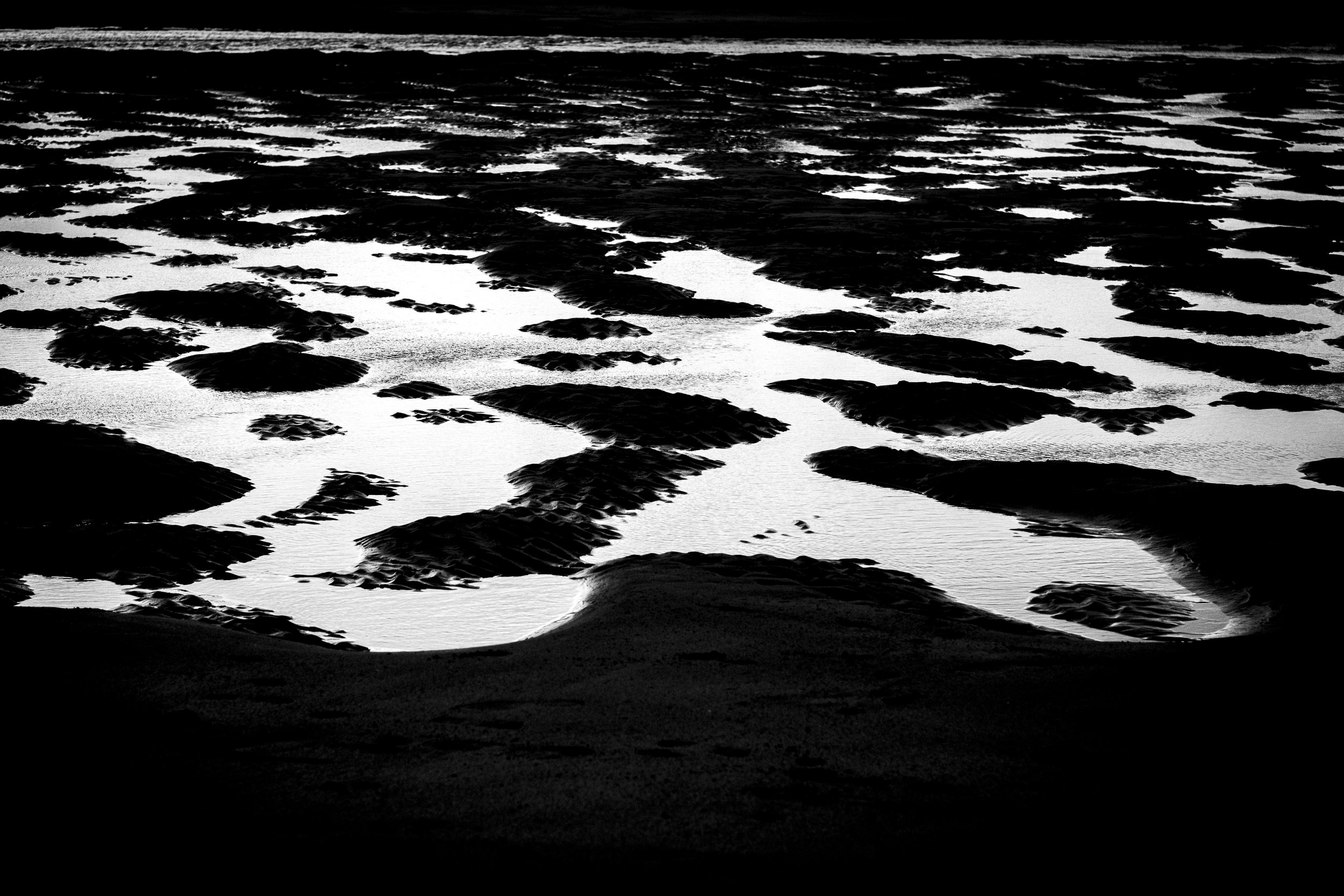 Black and white photo of rocks and water on a shoreline, with waves in the background.