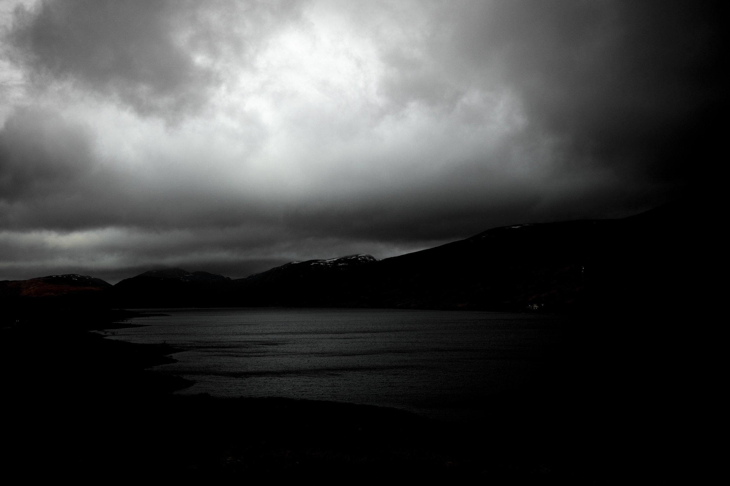 Dark, cloudy sky over mountains and a body of water at sunset or dusk.