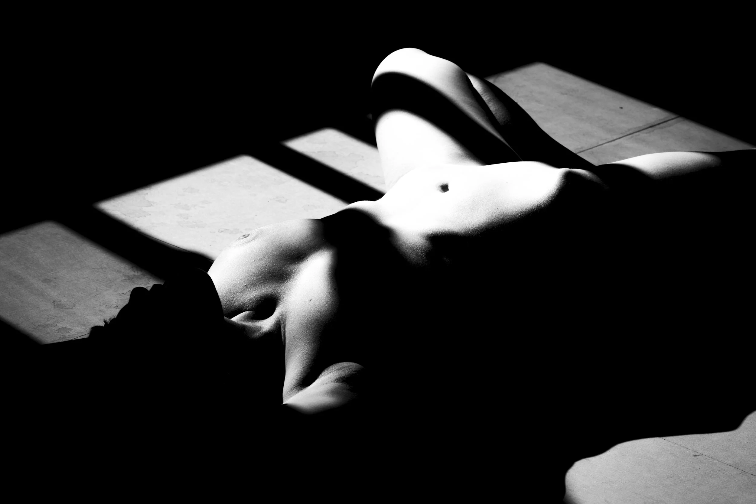 Black and white photo of a person lying on the ground in a shadow.