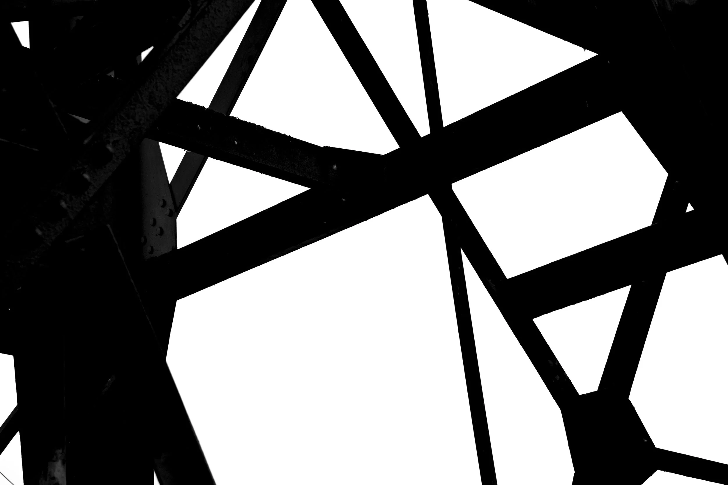 Black metal framework structure viewed from below against a white sky.