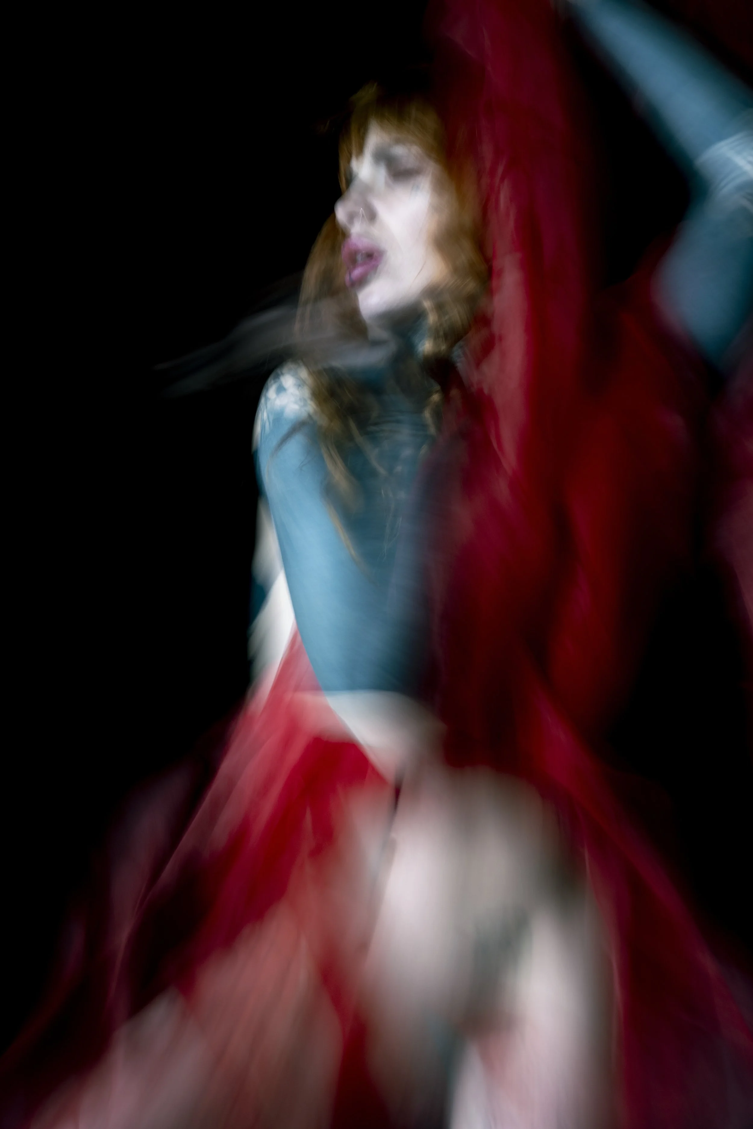 A blurred image of a woman with red hair, with her eyes closed, against a dark background.