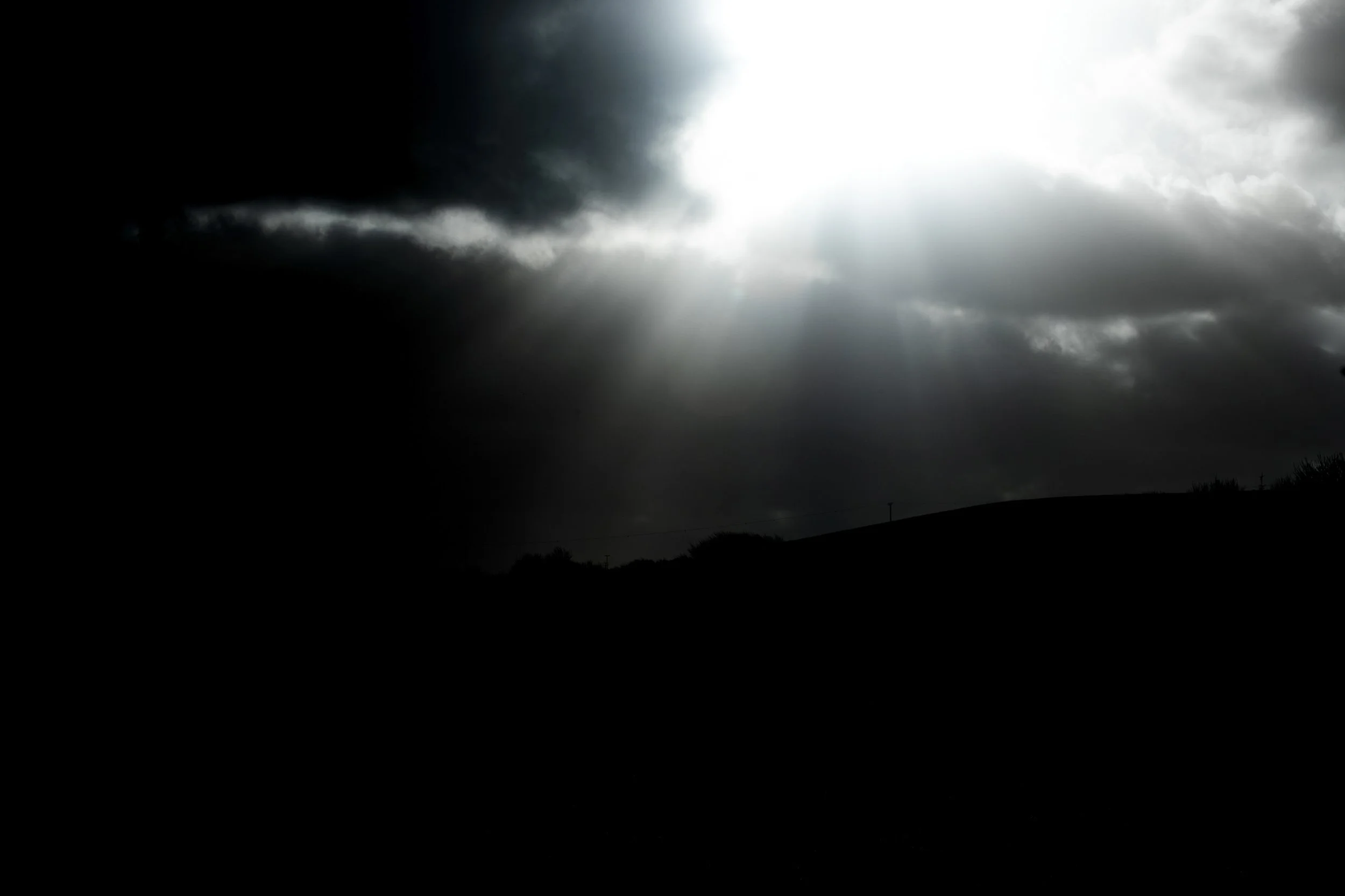 Dark storm clouds with a break in the clouds letting in bright light over a silhouetted landscape.