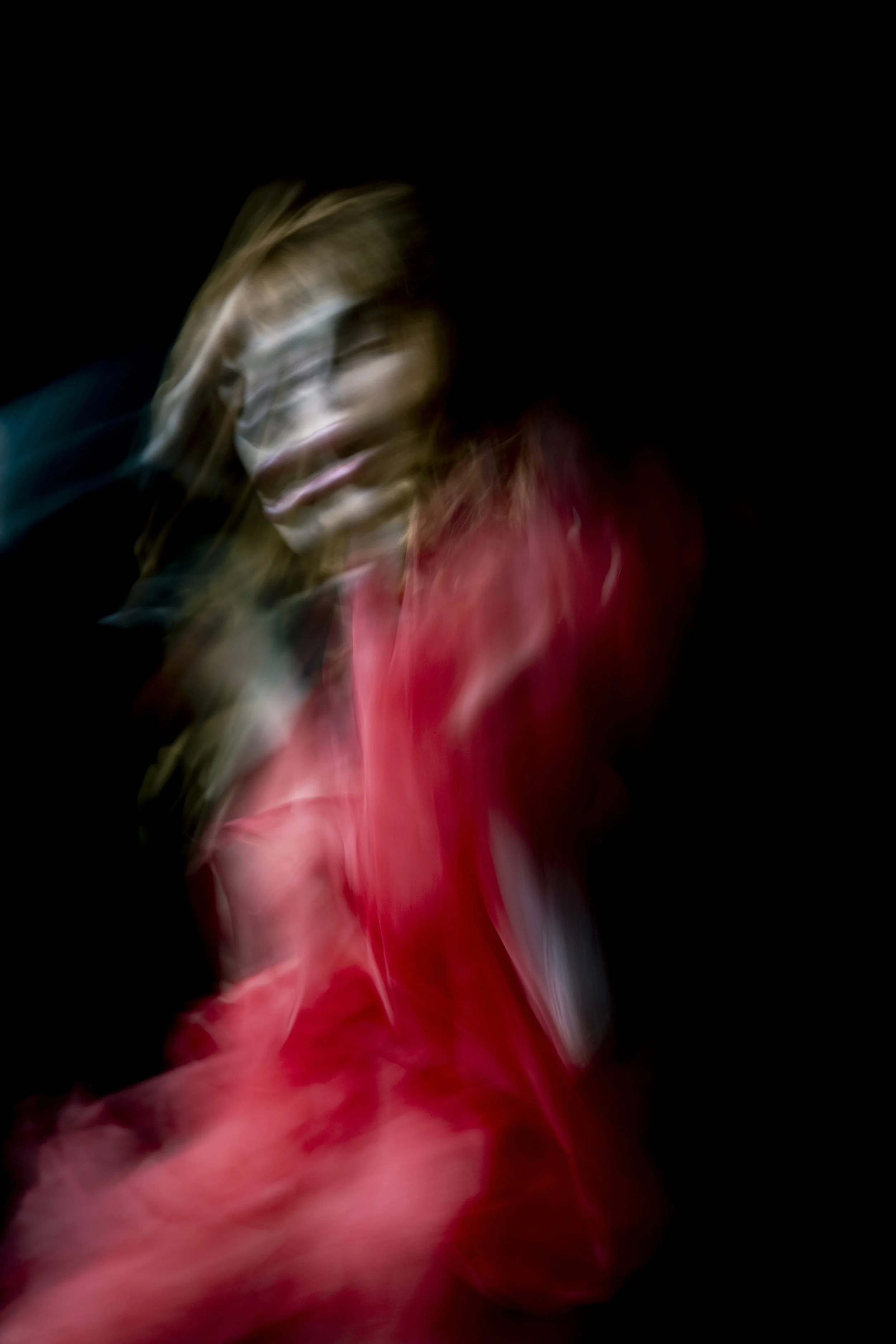 Abstract motion blur of a person with long hair wearing a red shirt against a black background.