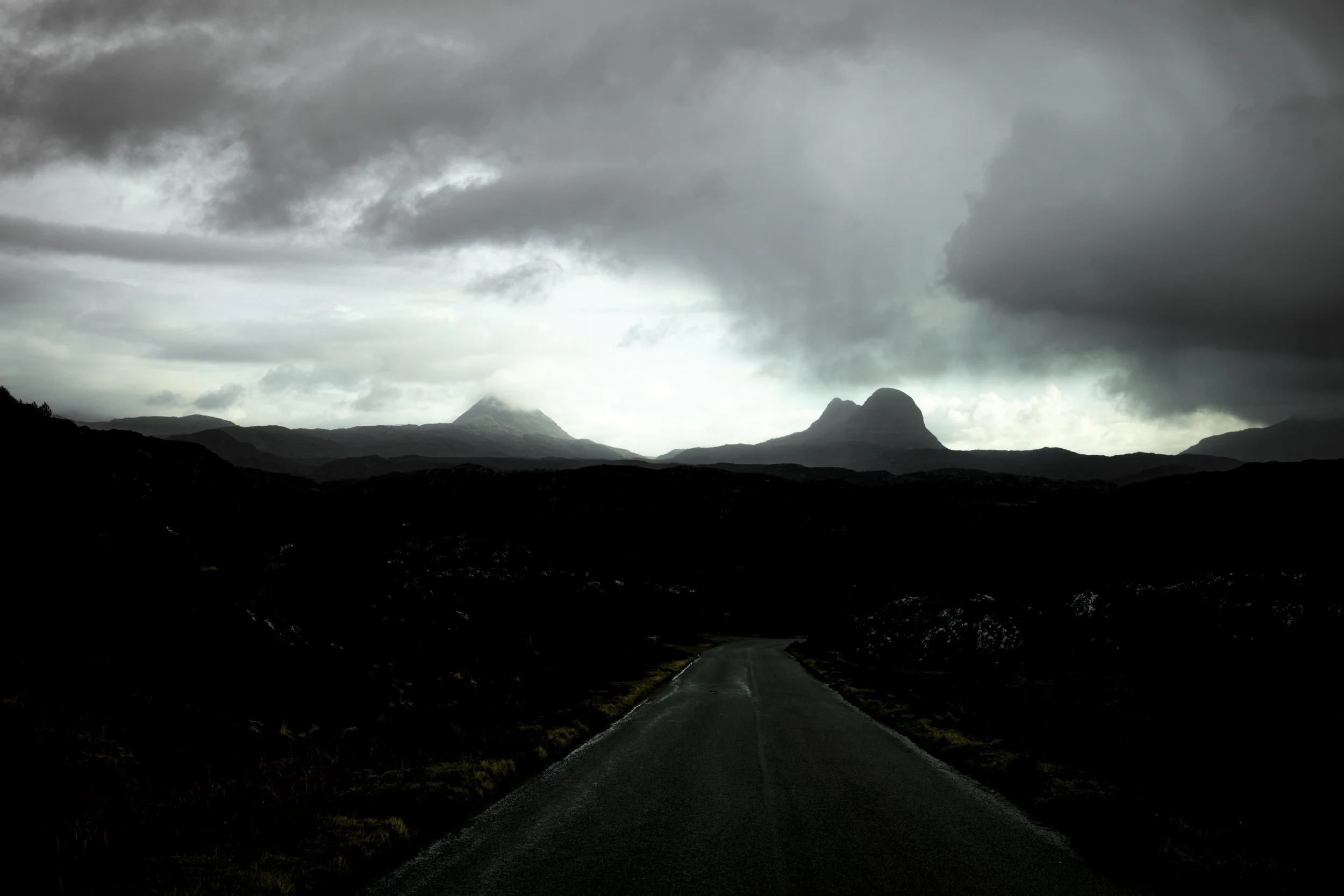 Dark clouds over mountain range with a winding road in the foreground.