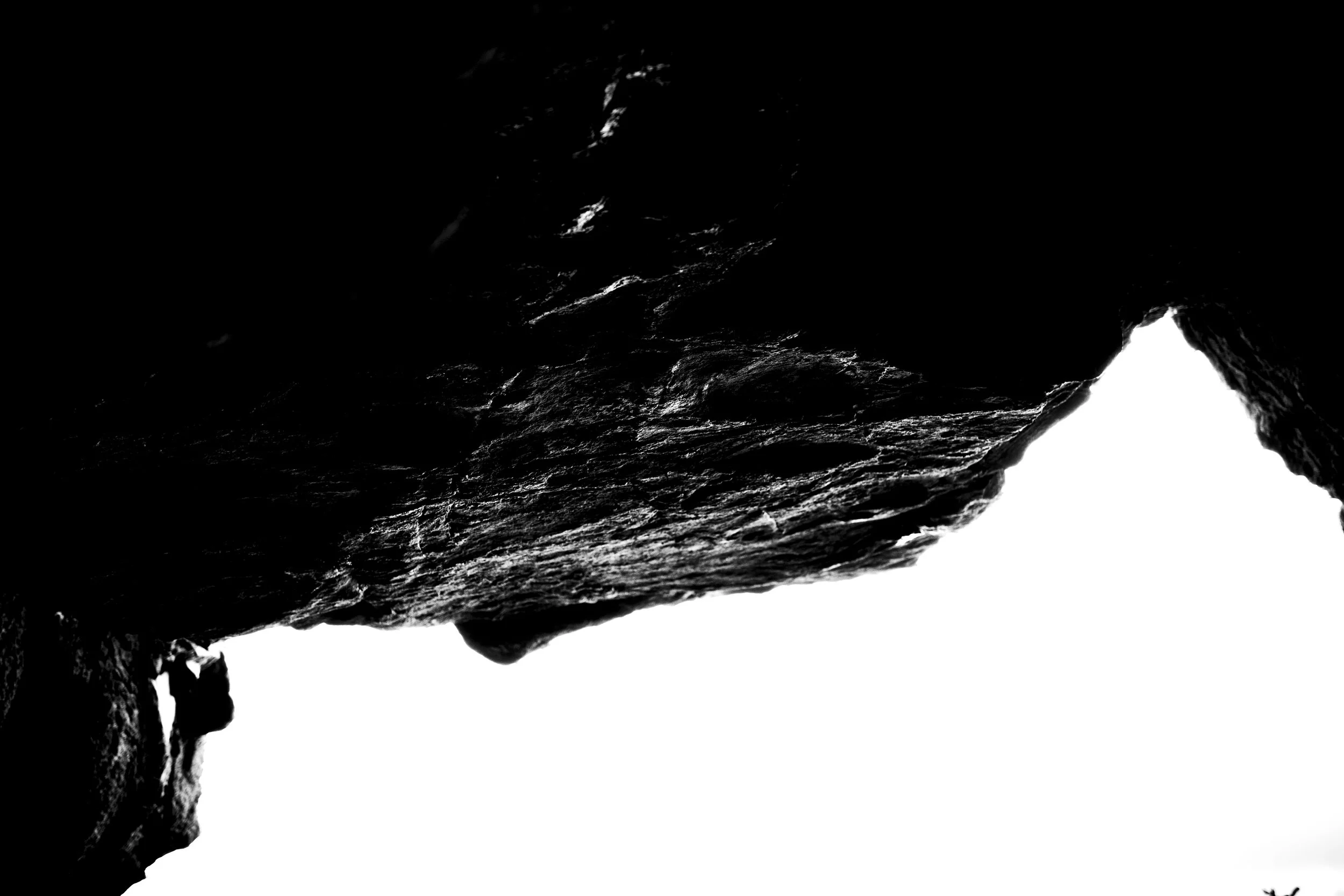 Close-up of a dark, rocky cliff with a small waterfall cascading down, highlighted by a stark contrast to the white background.