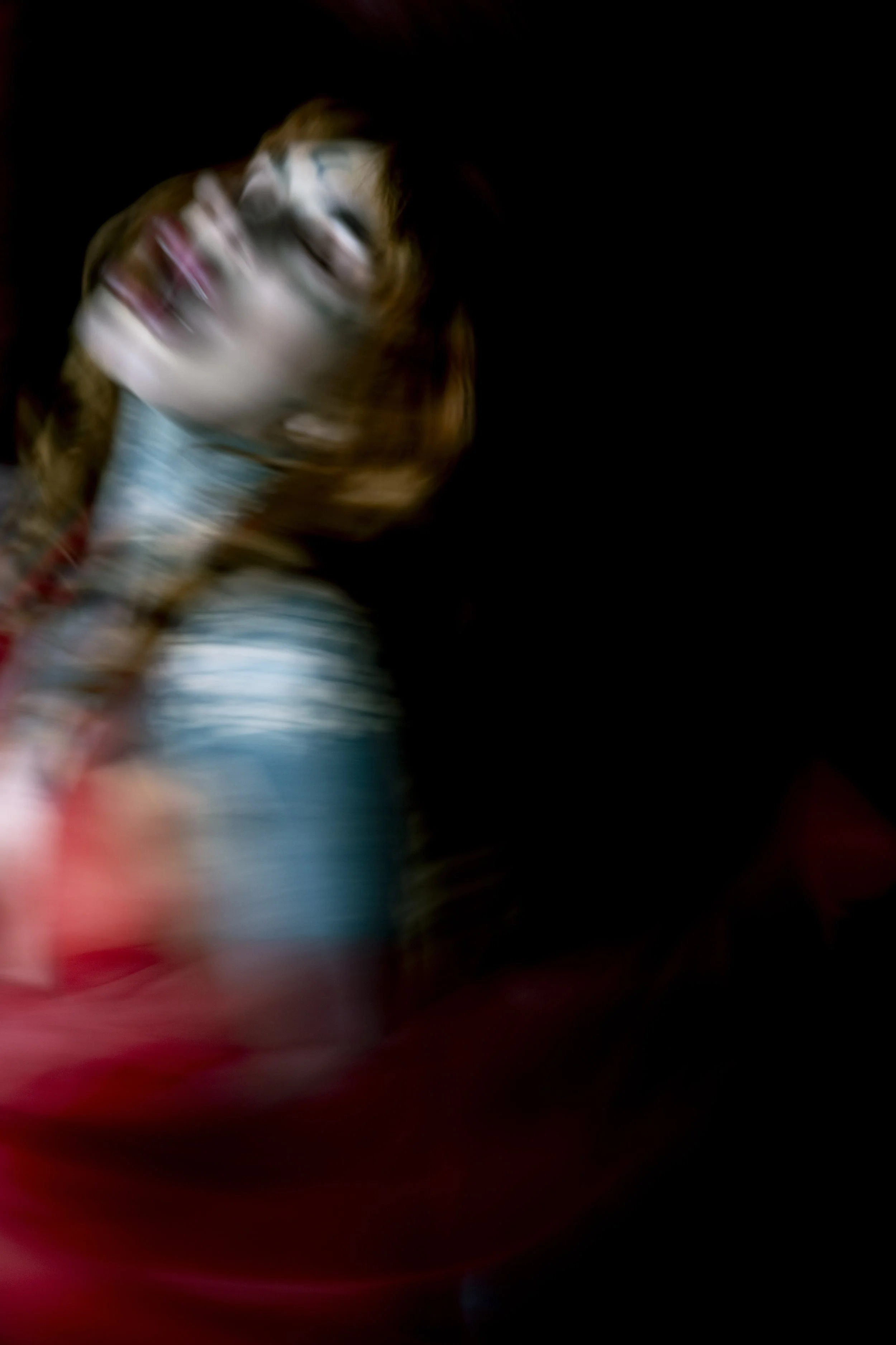 A blurry close-up photo of a person's face with long hair, against a dark background.