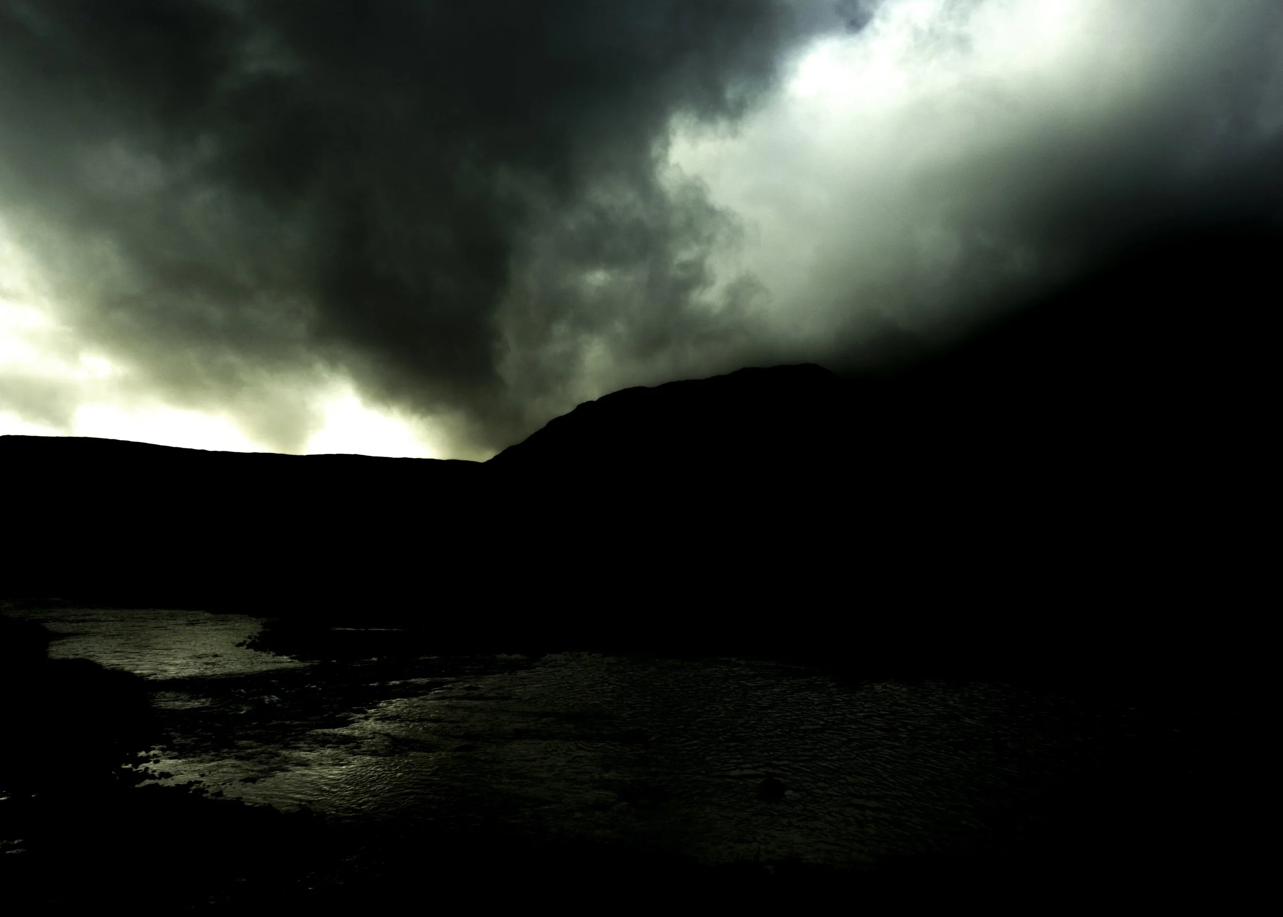 Dark stormy clouds over a silhouette of a mountain and the ocean at night