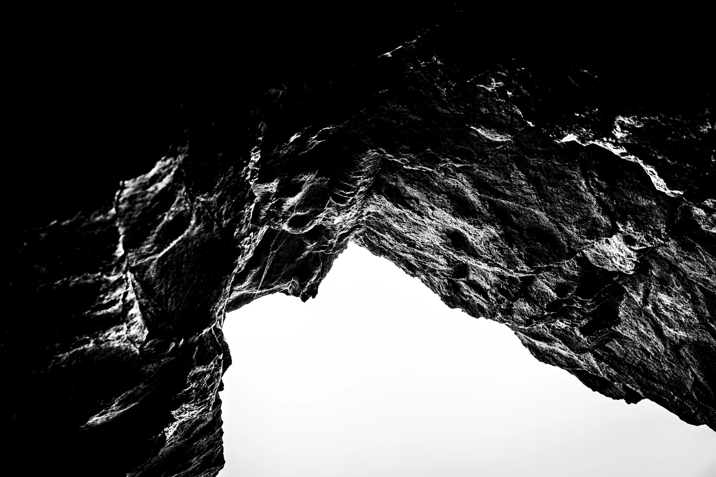 Black and white photograph looking upward through a narrow canyon or rock formation towards the sky.