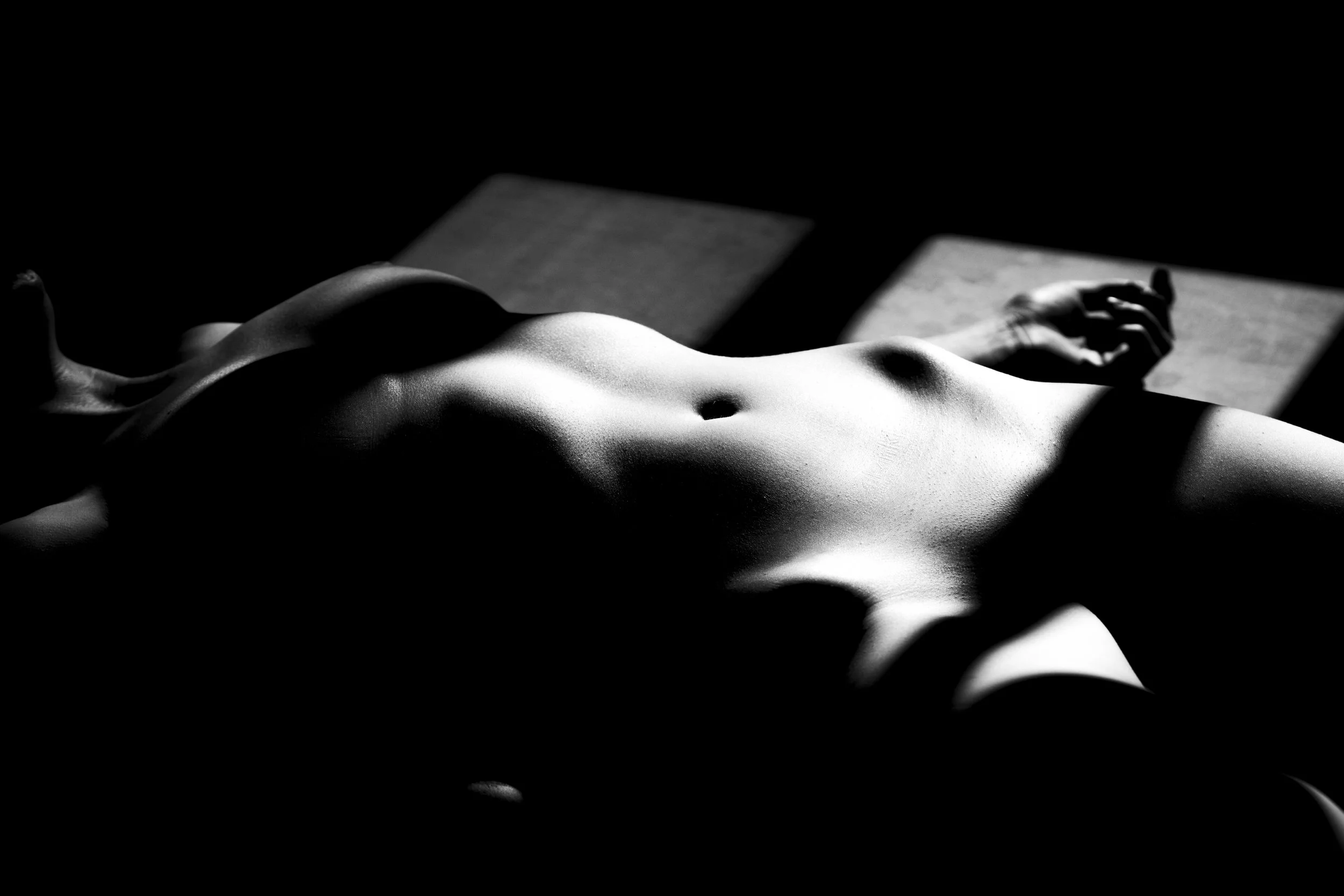 Black and white photo of a human nude lying on a surface, with dramatic shadows and lighting highlighting the body contours.