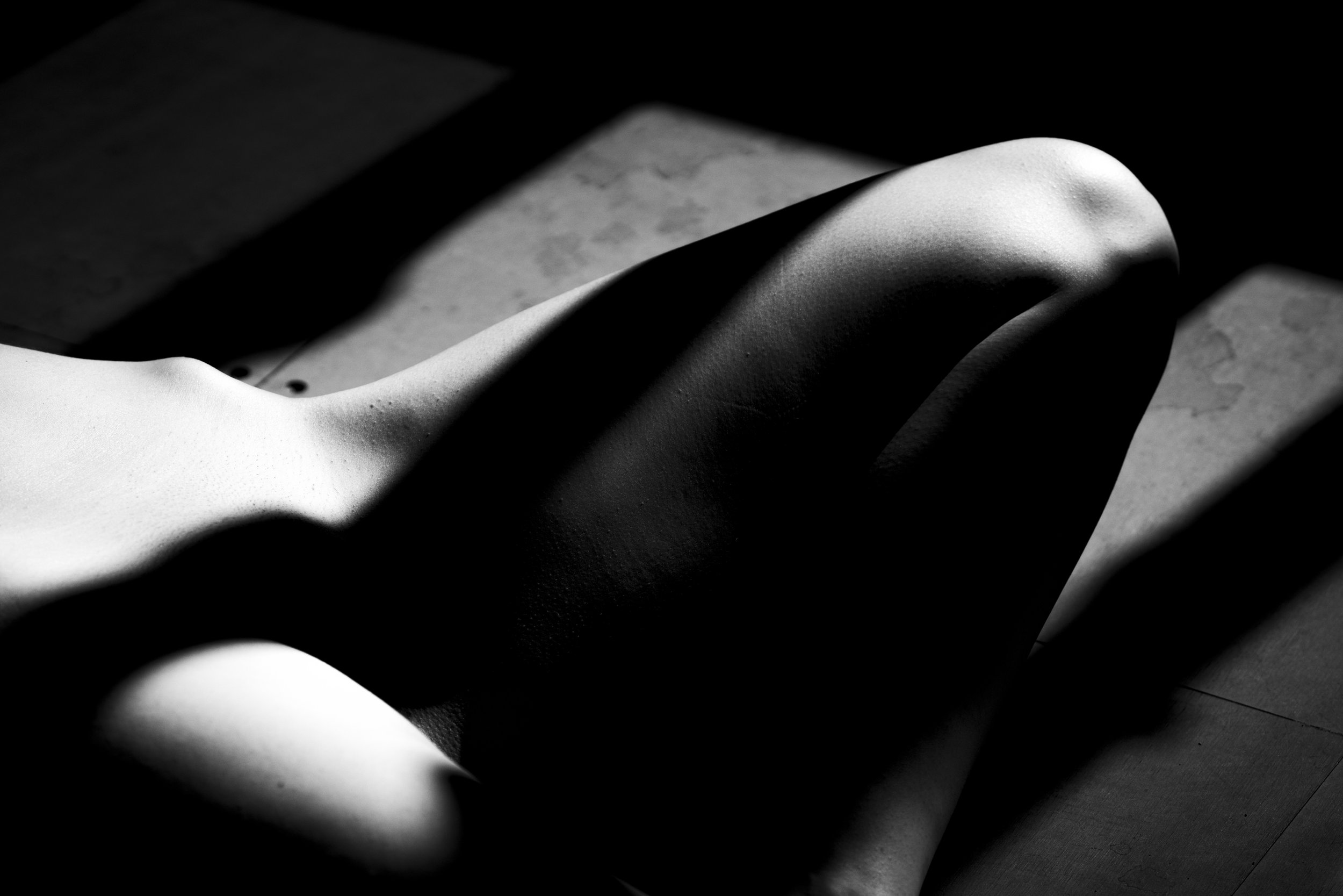 Close-up of a human body with a focus on the back, illuminated with dramatic lighting, showing smooth skin and muscular contours, in a black and white photograph.