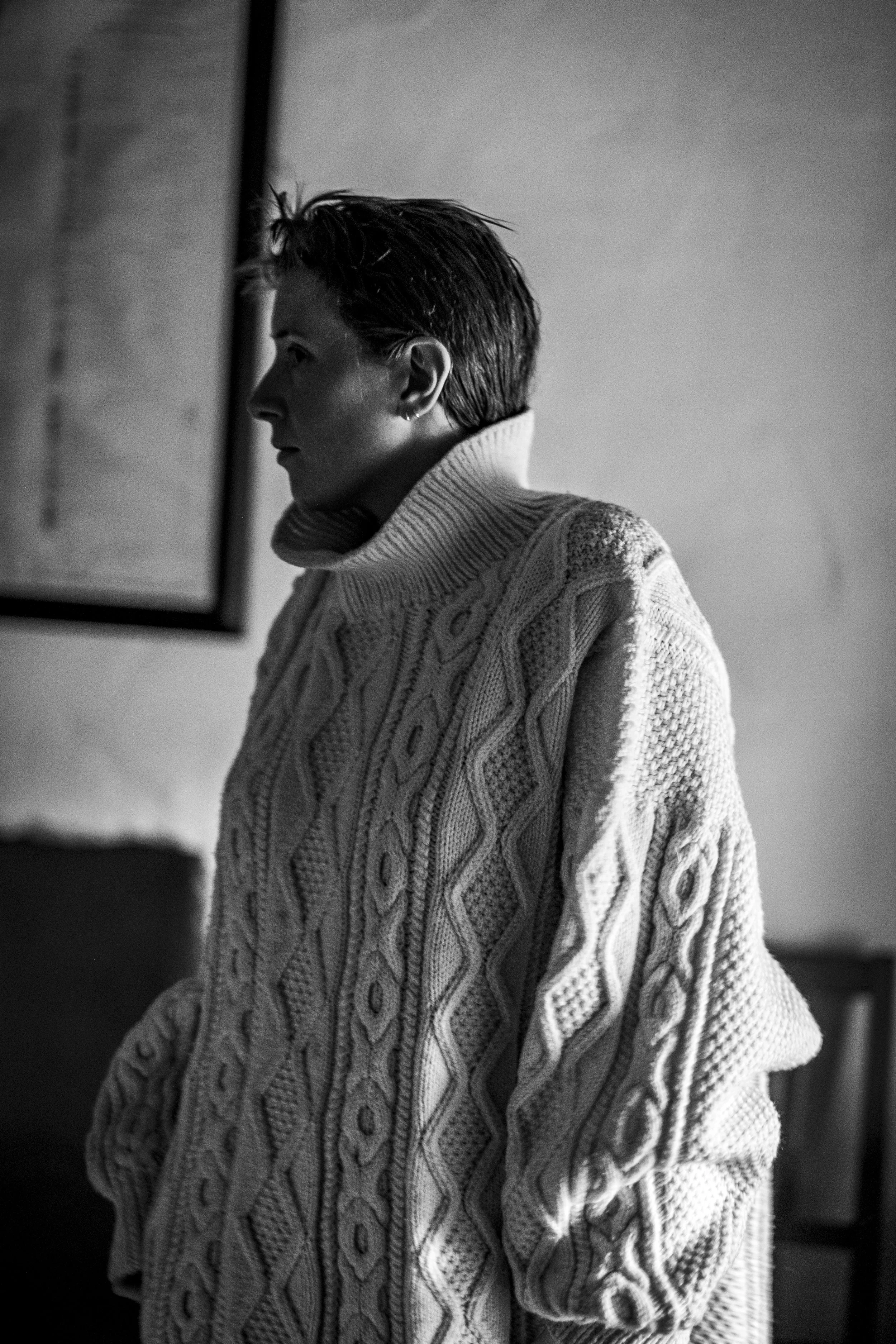 A woman in a cable-knit sweater with short hair looking to the side in black and white.