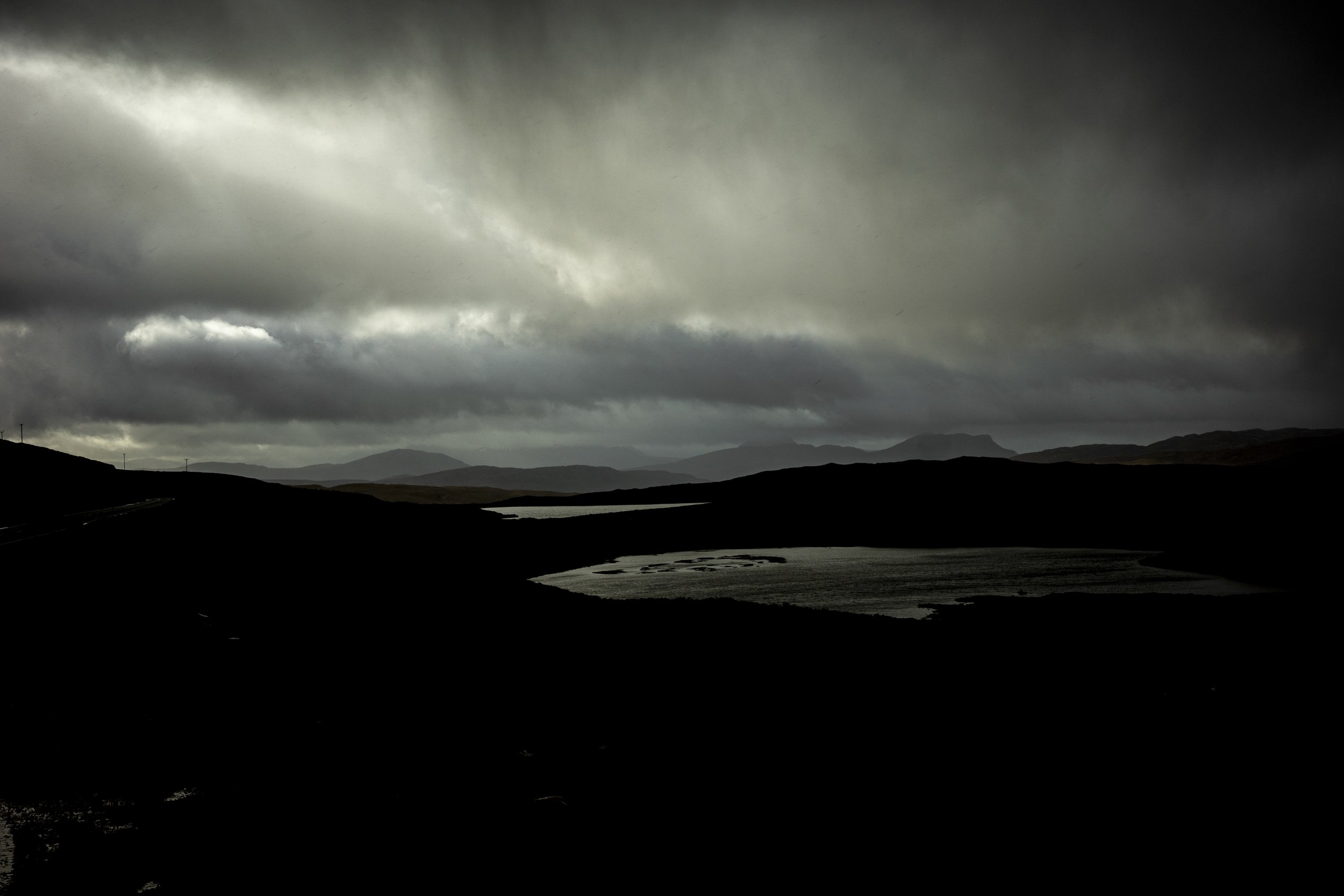 Dark, cloudy sky over a mountainous landscape with a body of water in the foreground.