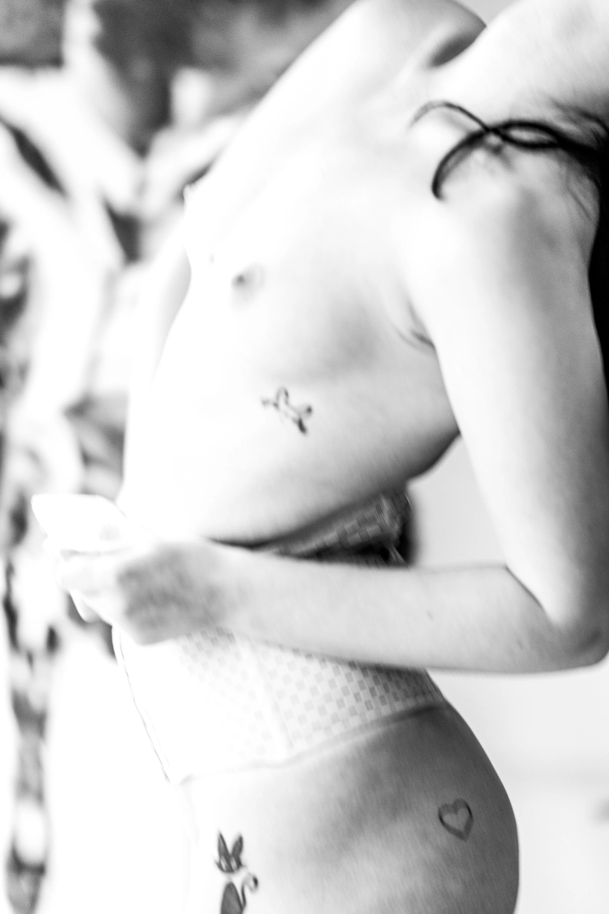 Close-up of a person's arm and hand resting on a table, with a heart-shaped tattoo visible on the forearm, in black and white.