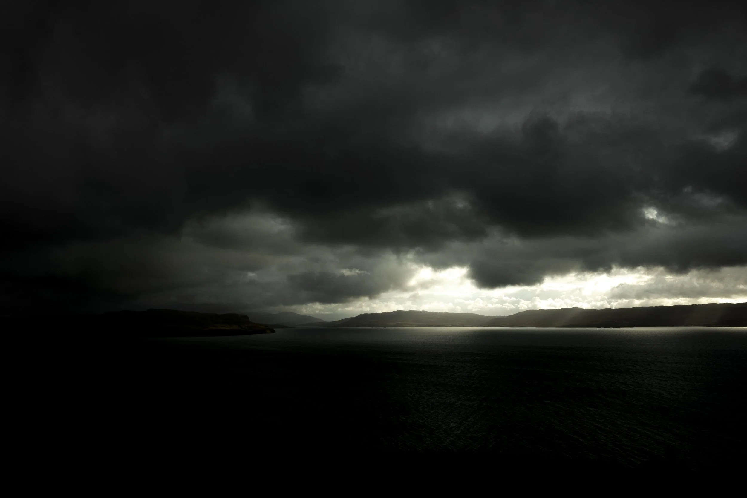 Dark storm clouds over a body of water with mountains in the background.