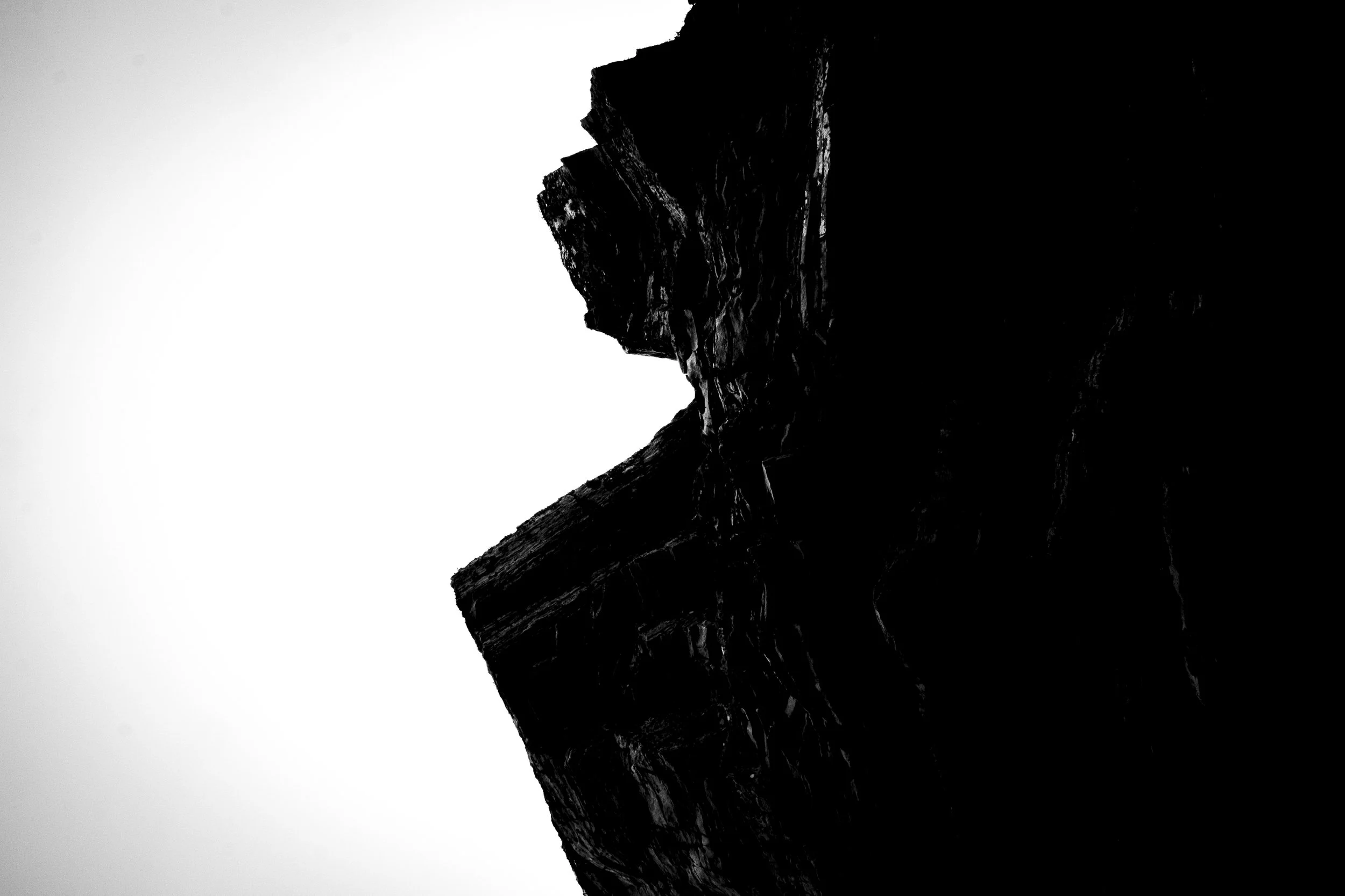 Silhouette of a mountain or rock formation against a light gradient background.