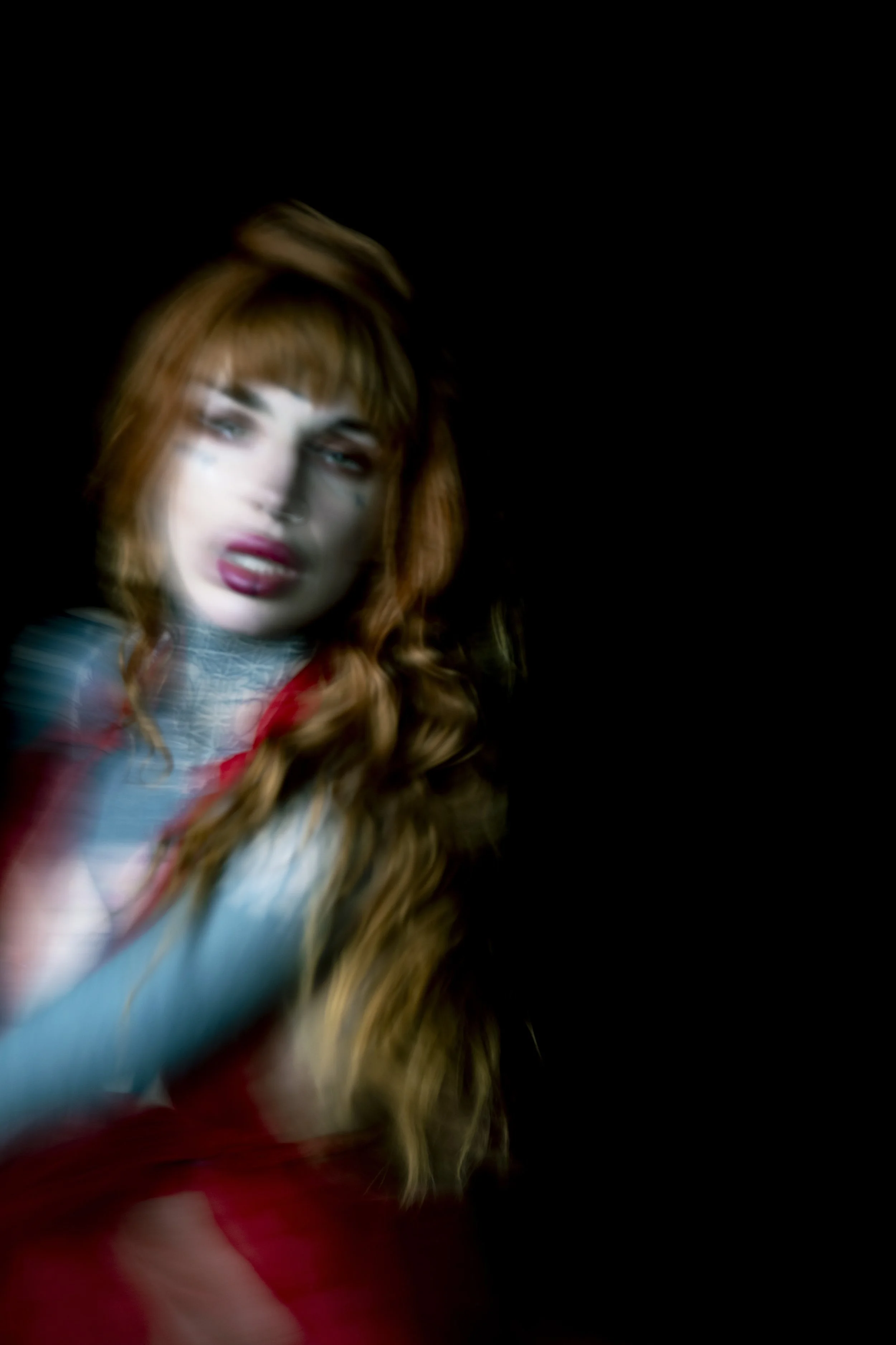 A blurry close-up of a woman with red hair, set against a dark background.